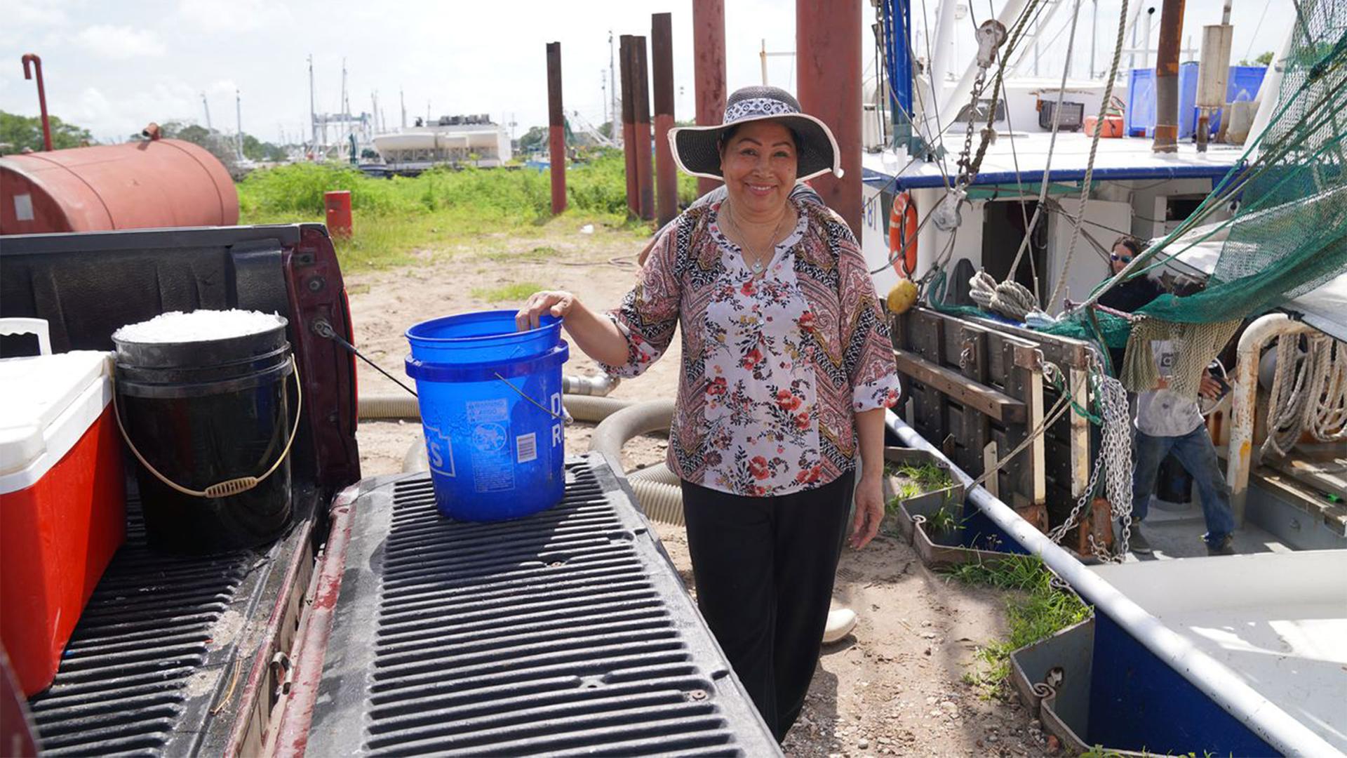 A woman wearing a hat stands next to a blue bucket