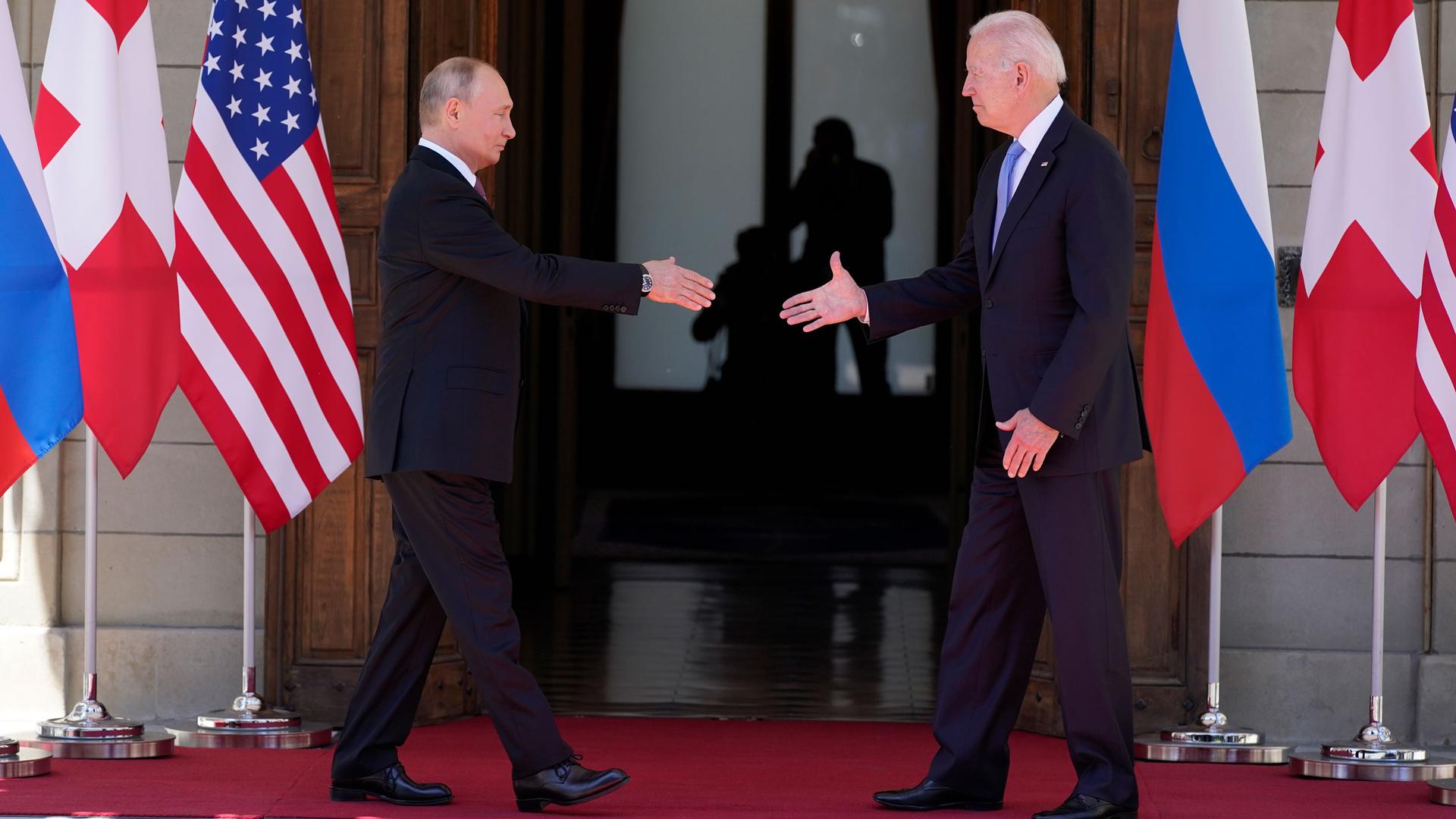 President Joe Biden and Russian President Vladimir Putin are shown walking toward each other with their hands outstretched for a shake.