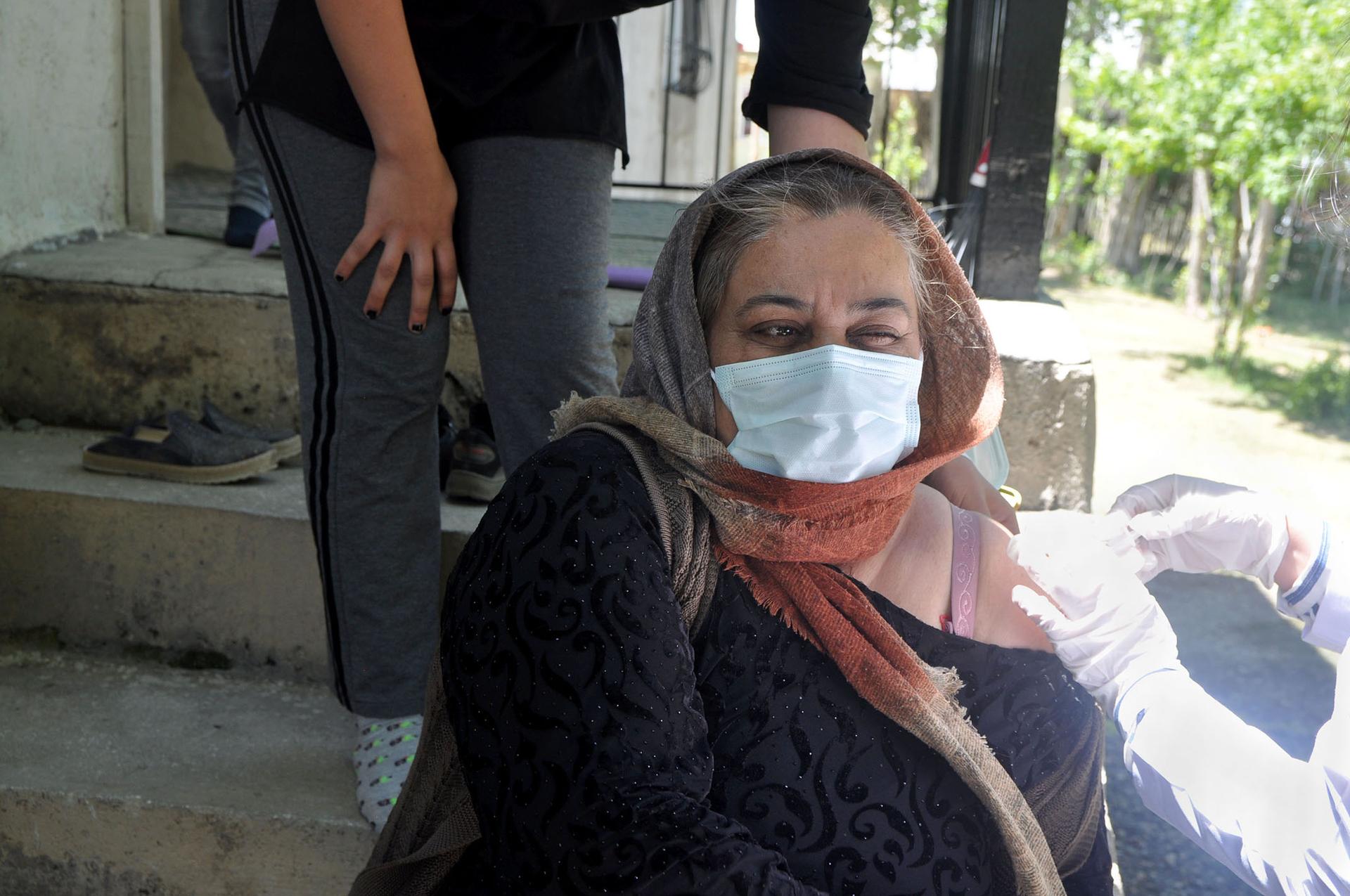Emine Saruhan winces during a COVID vaccination shot on her front porch in the town of Ömerova. The 46-year-old has a health condition, and hoped a vaccine would alleviate some of her fears.