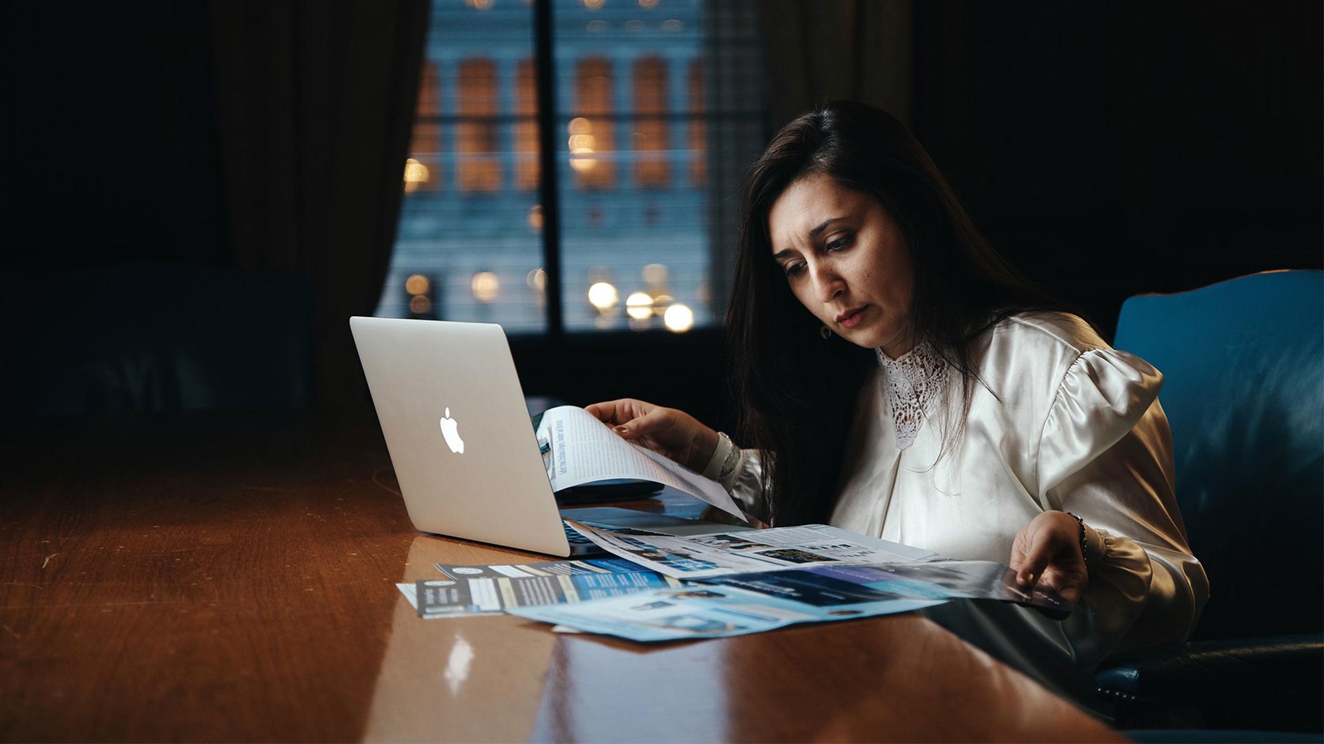 Woman in a white blouse working at a desk on her laptop