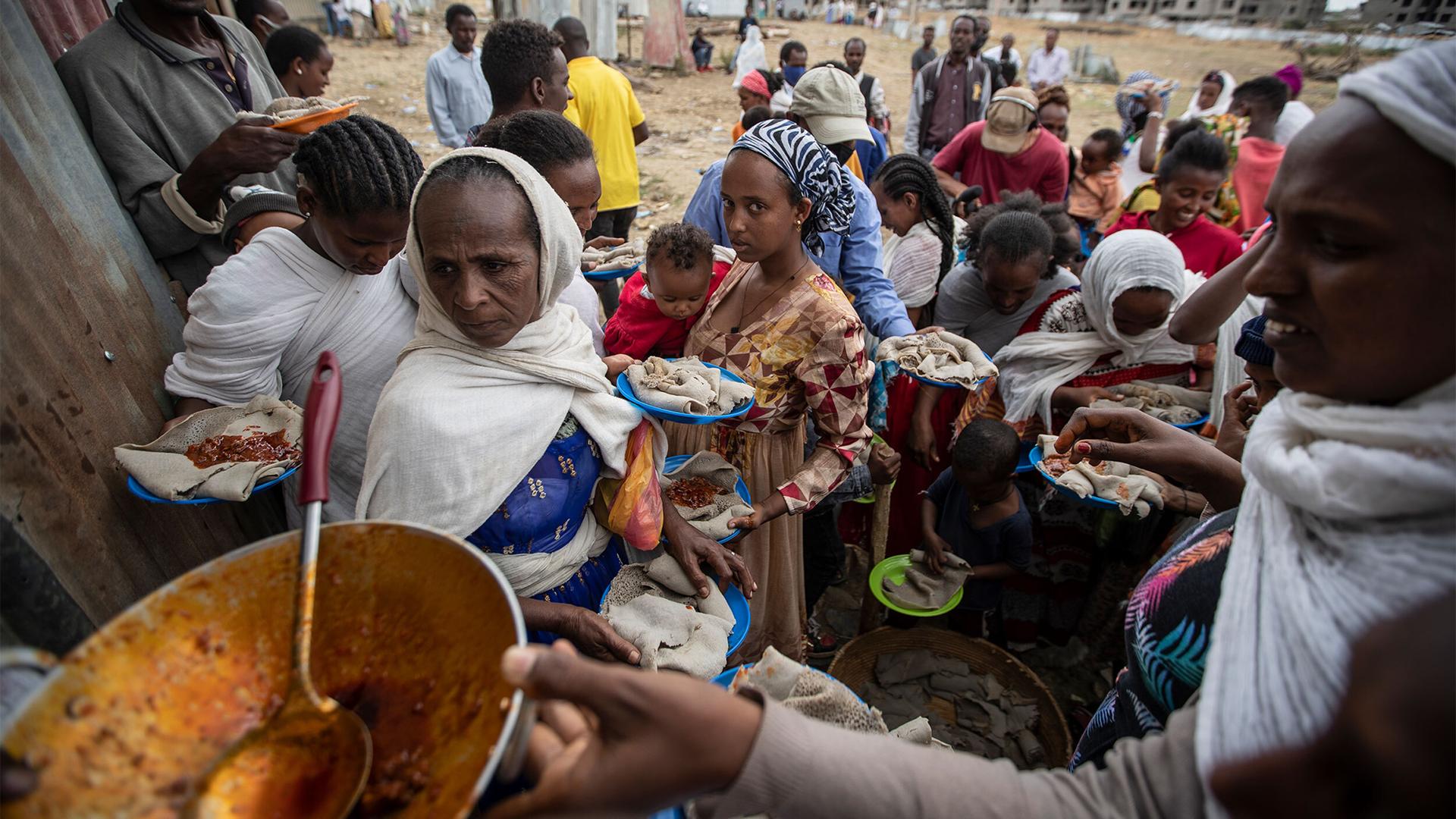 A group of people are shown waiting in line where plates of traditional Ethiopian food are being served.
