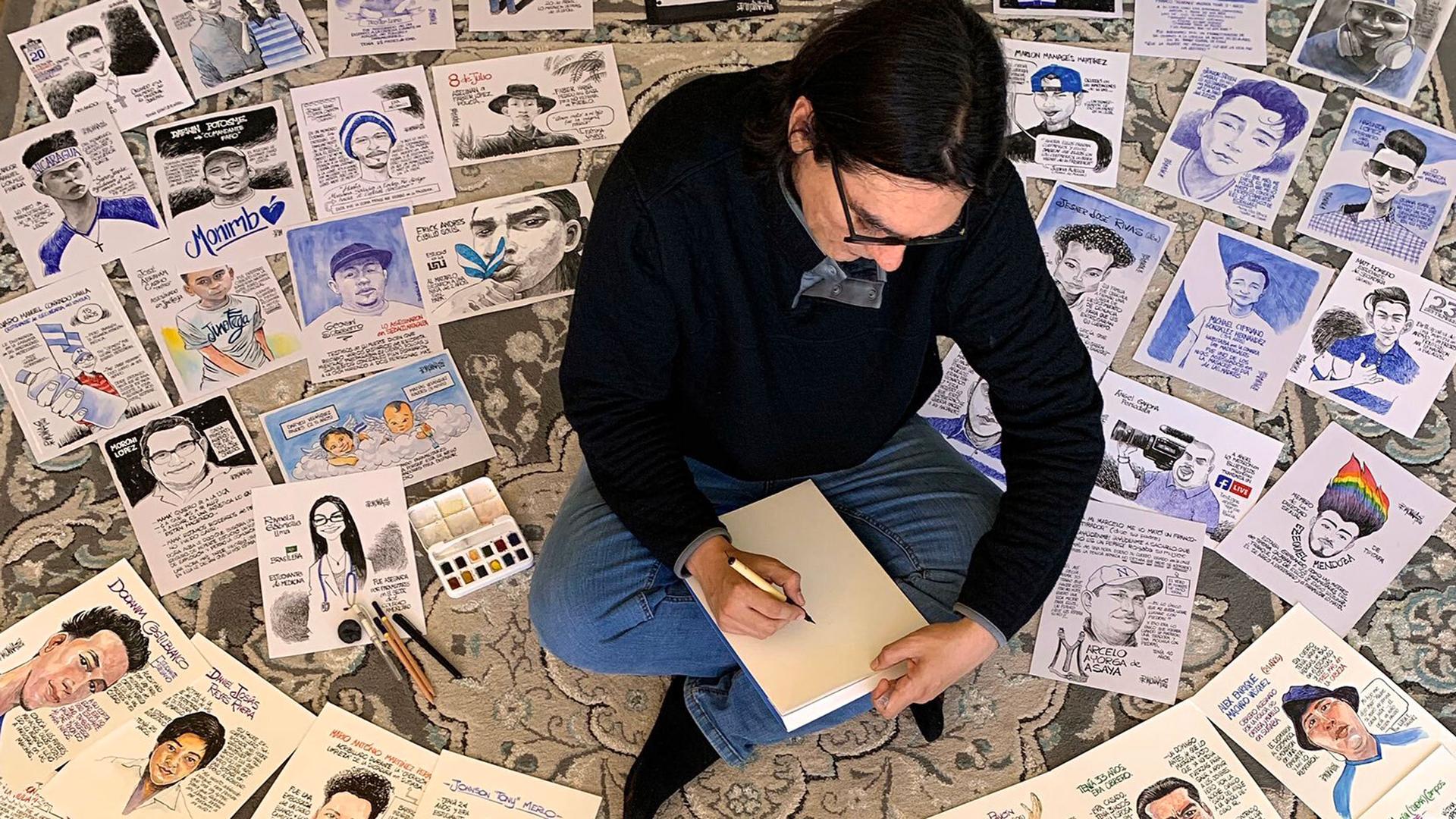 A man is shown sitting cross-legged with dozens of cartoons on the floor all around him.