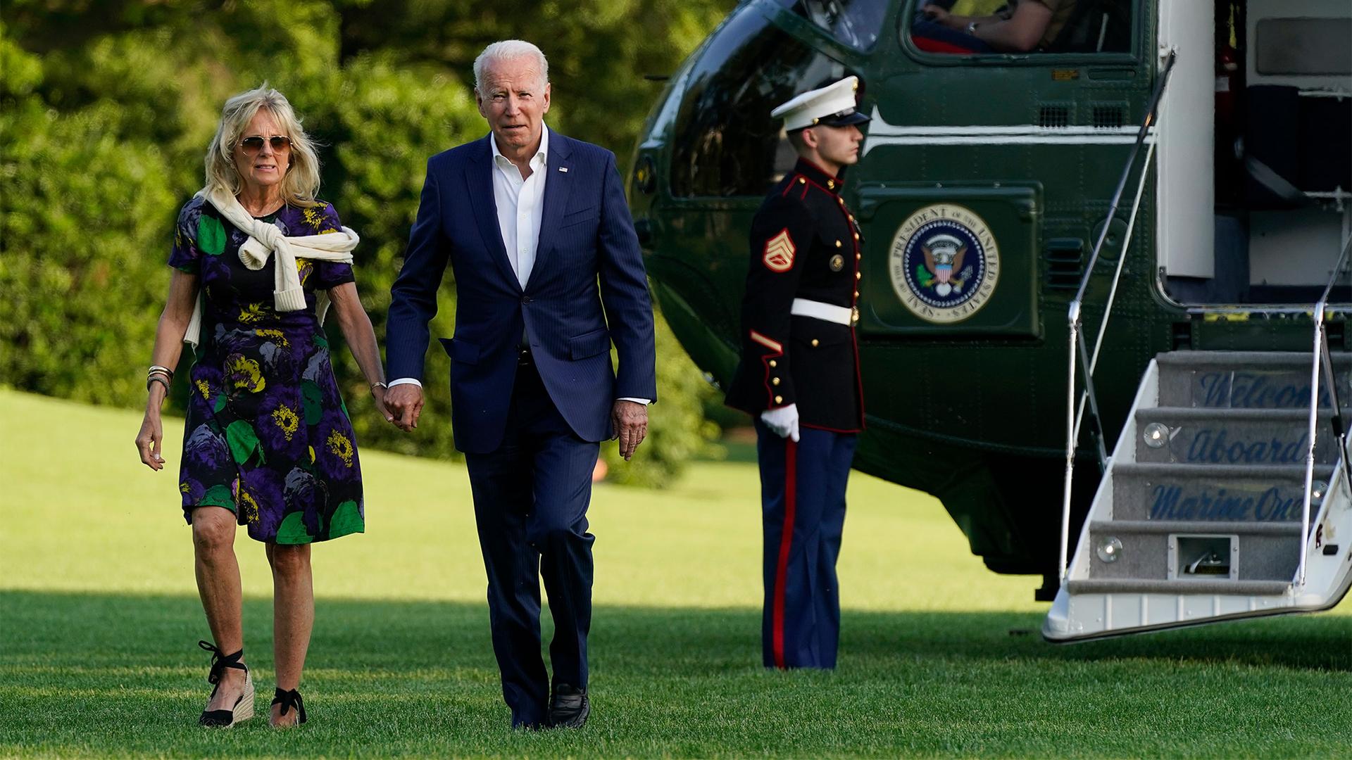 President Biden in a blue suit and First Lady Jill Biden in a purple, green, yellow and black dress walk past Marine One