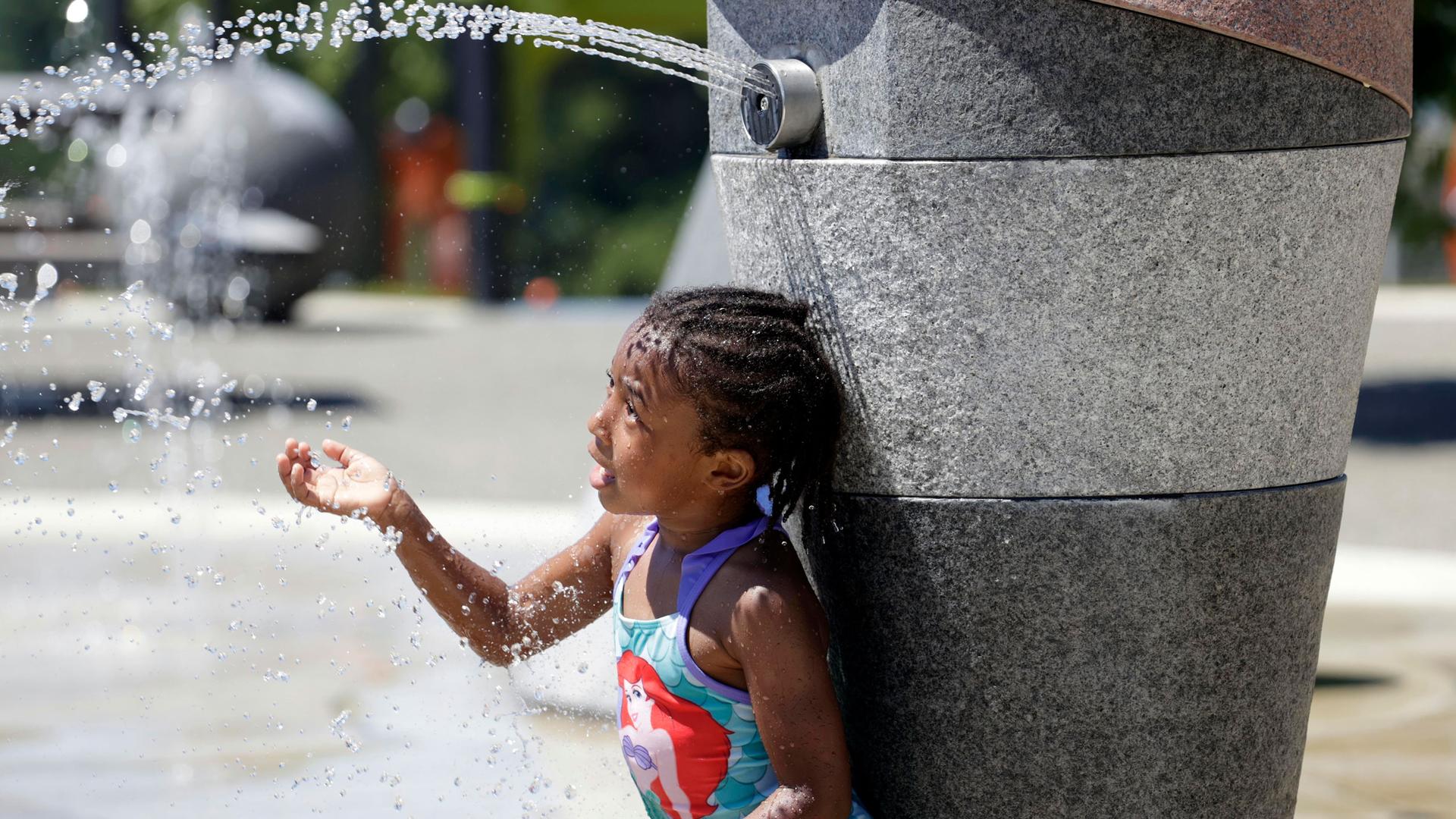 A young girl is shown leaning up against a stone column spraying a stream of water.