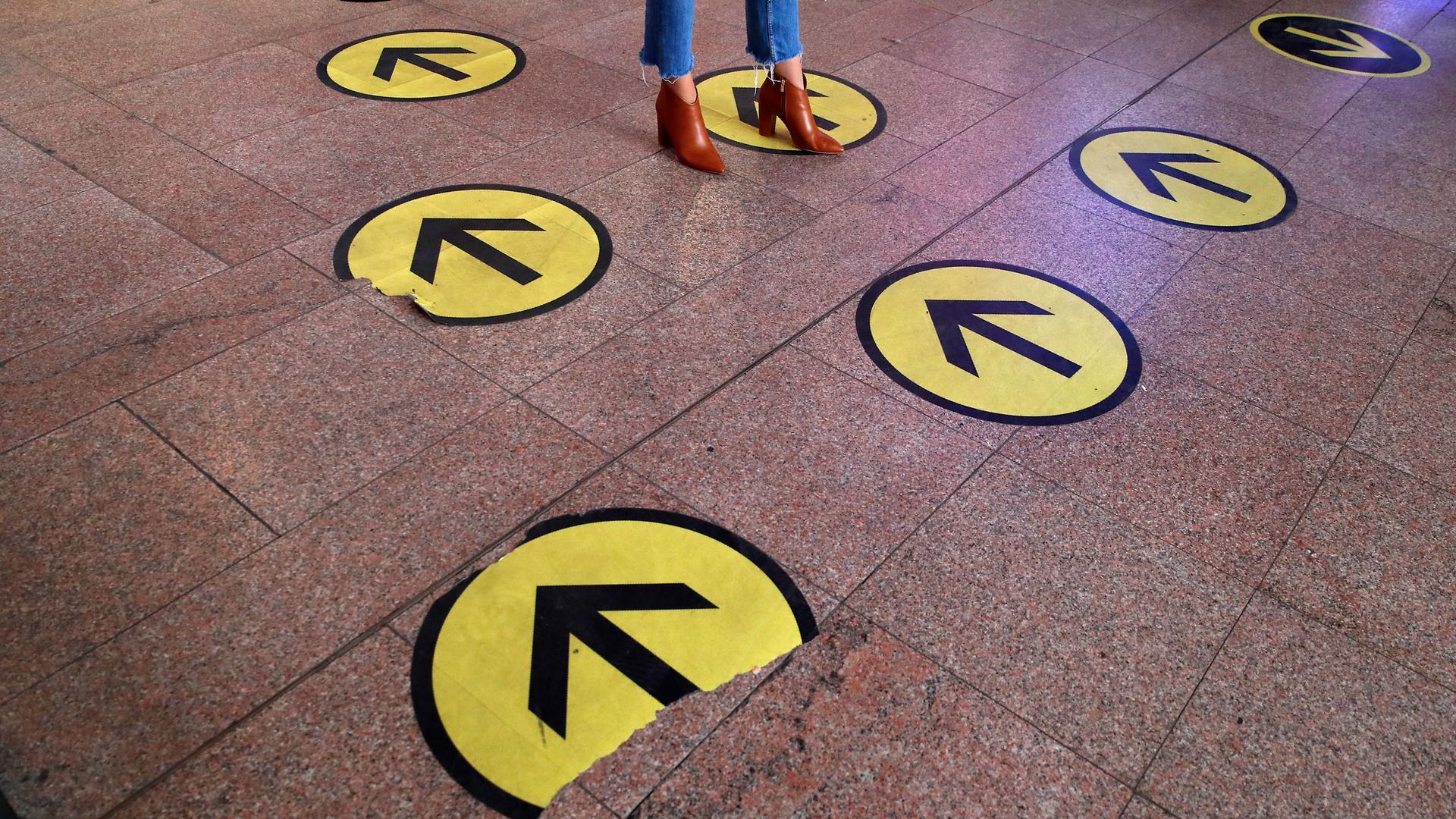 Several large stickers are shown on the floor with yellow and black arrows with a person standing on one arrow going the opposite direction.