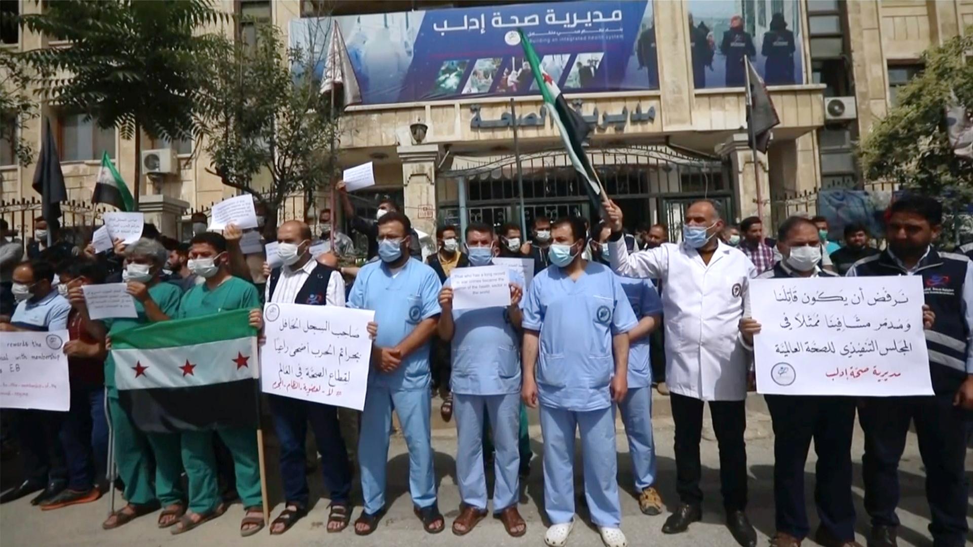 In this image taken from video, dozens of medical workers protest a decision to grant Syrian President Bashar al-Assad’s government a seat on the executive board of the World Health Organization, May 31, 2021, in Idlib, Syria.