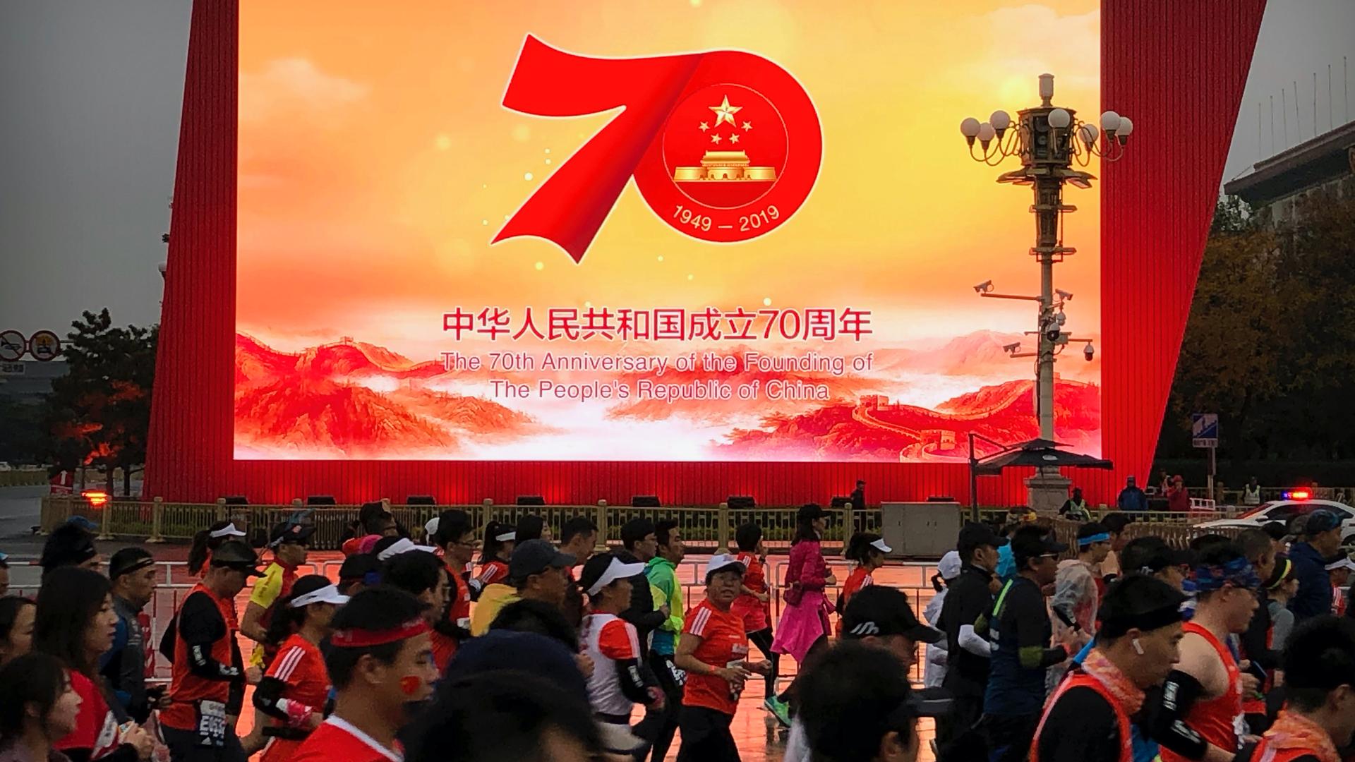 Runners pass by a large video screen commemorating the 70th anniversary of the founding of Communist China during the Beijing Marathon in Beijing, Nov. 3, 2019.