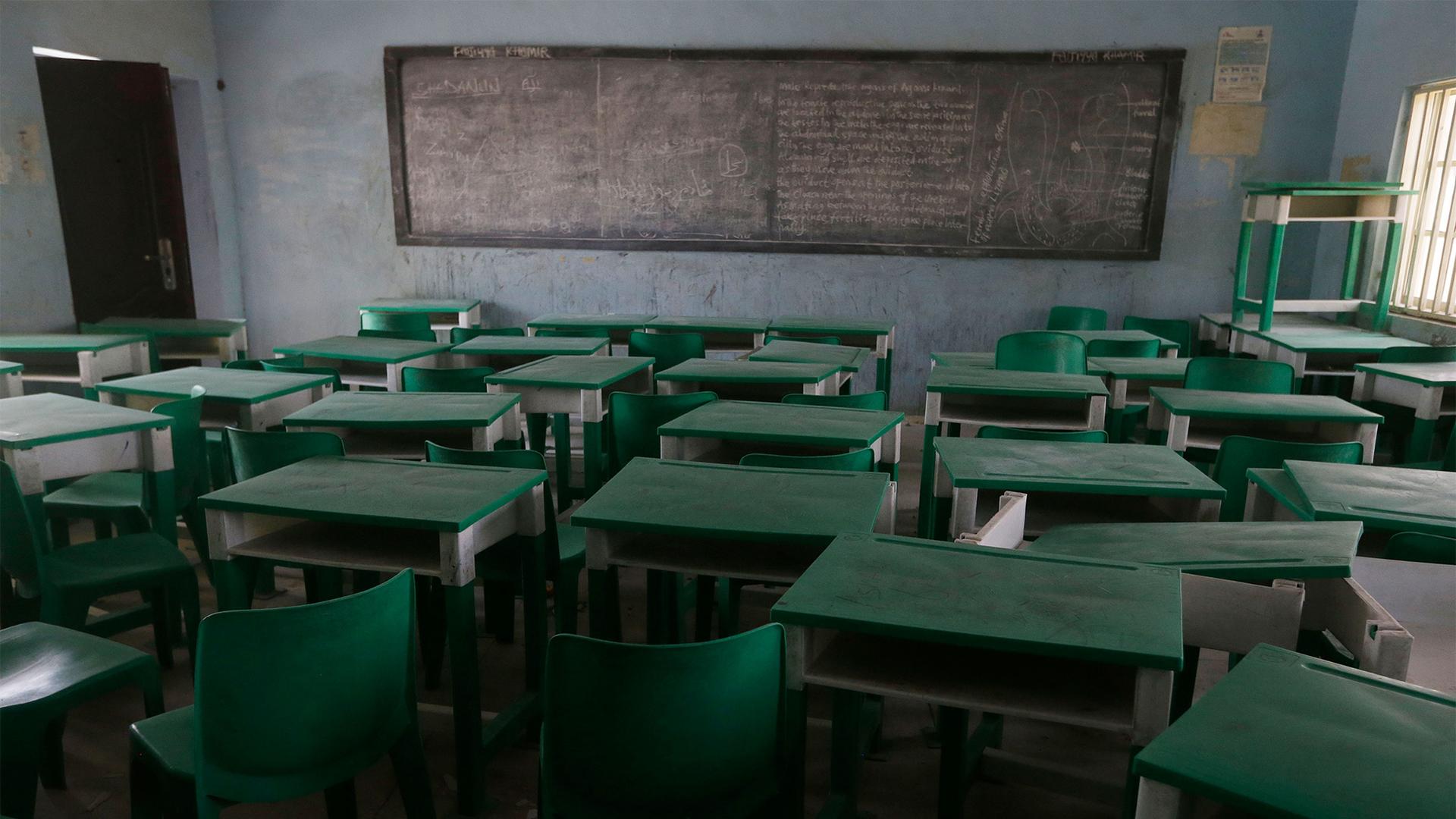 Empty green desks and chairs in a classroom with a chalkboard at the front