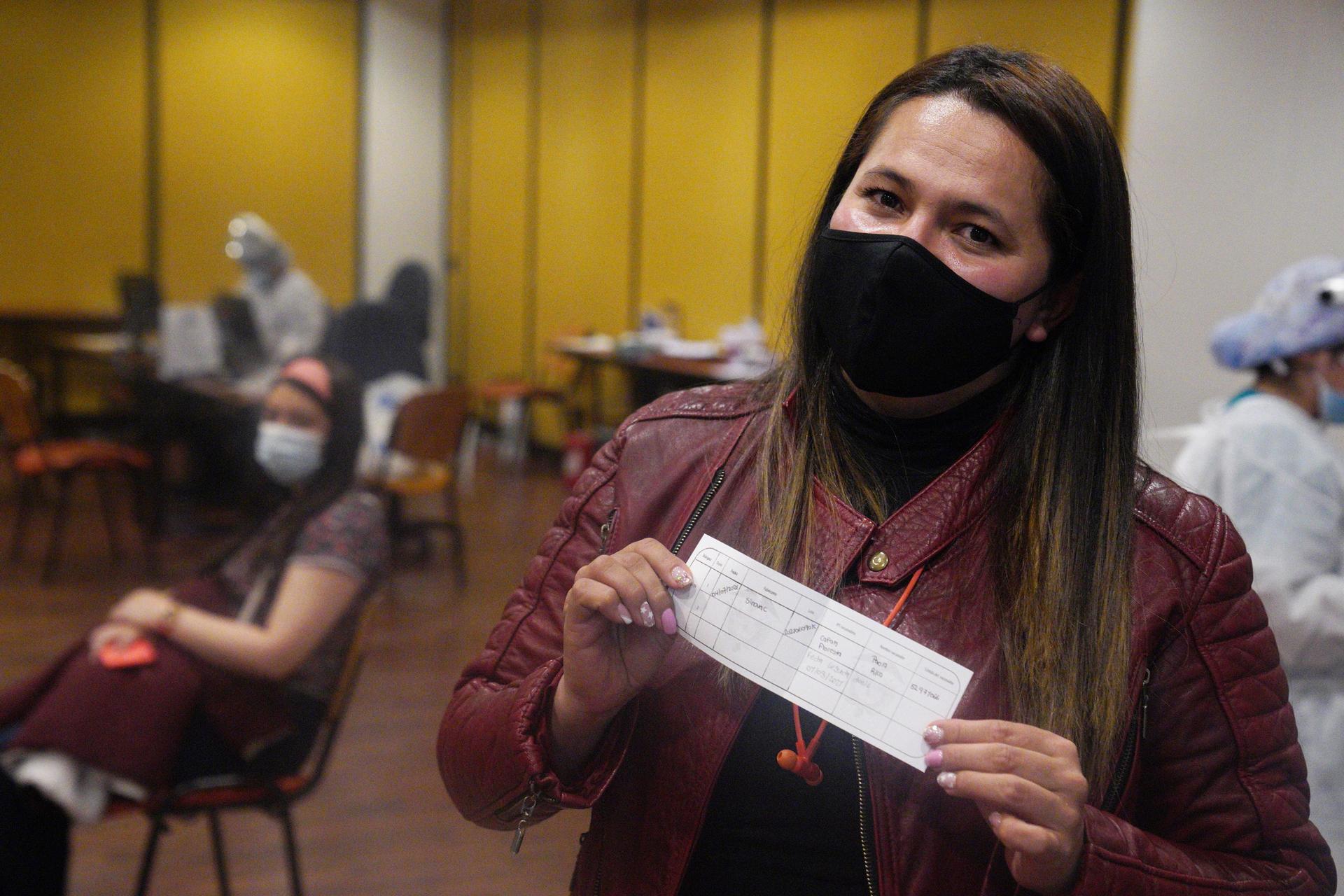 A masked woman holds up her vaccine certificate.