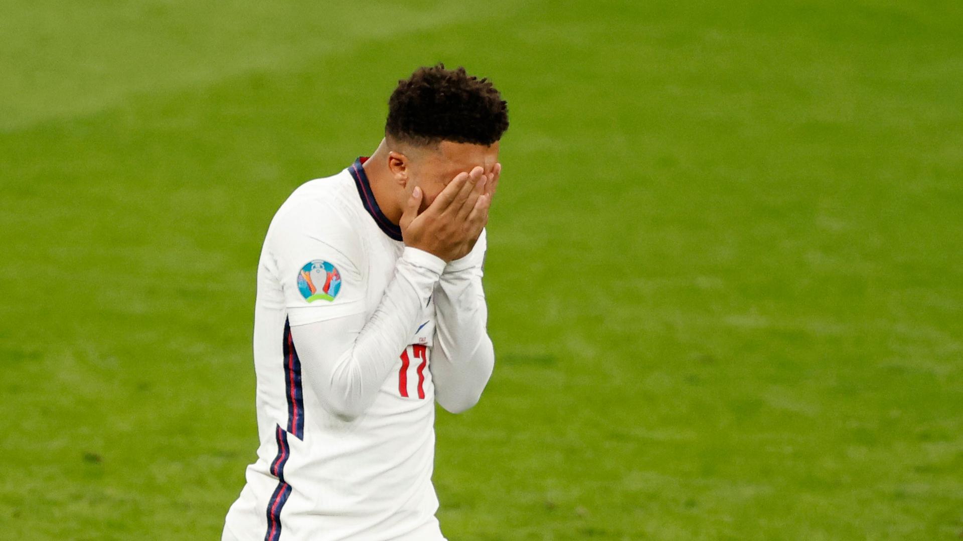 England's Jadon Sancho is shown on the soccer pitch holding his hands to his face.