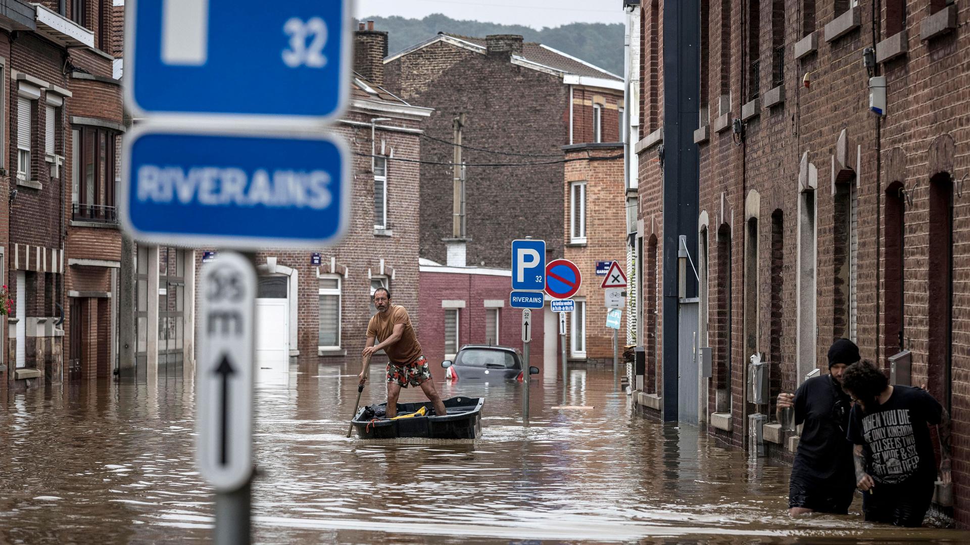 A man is shown standing in a canoe and rowing down an city street flooded by several feet.