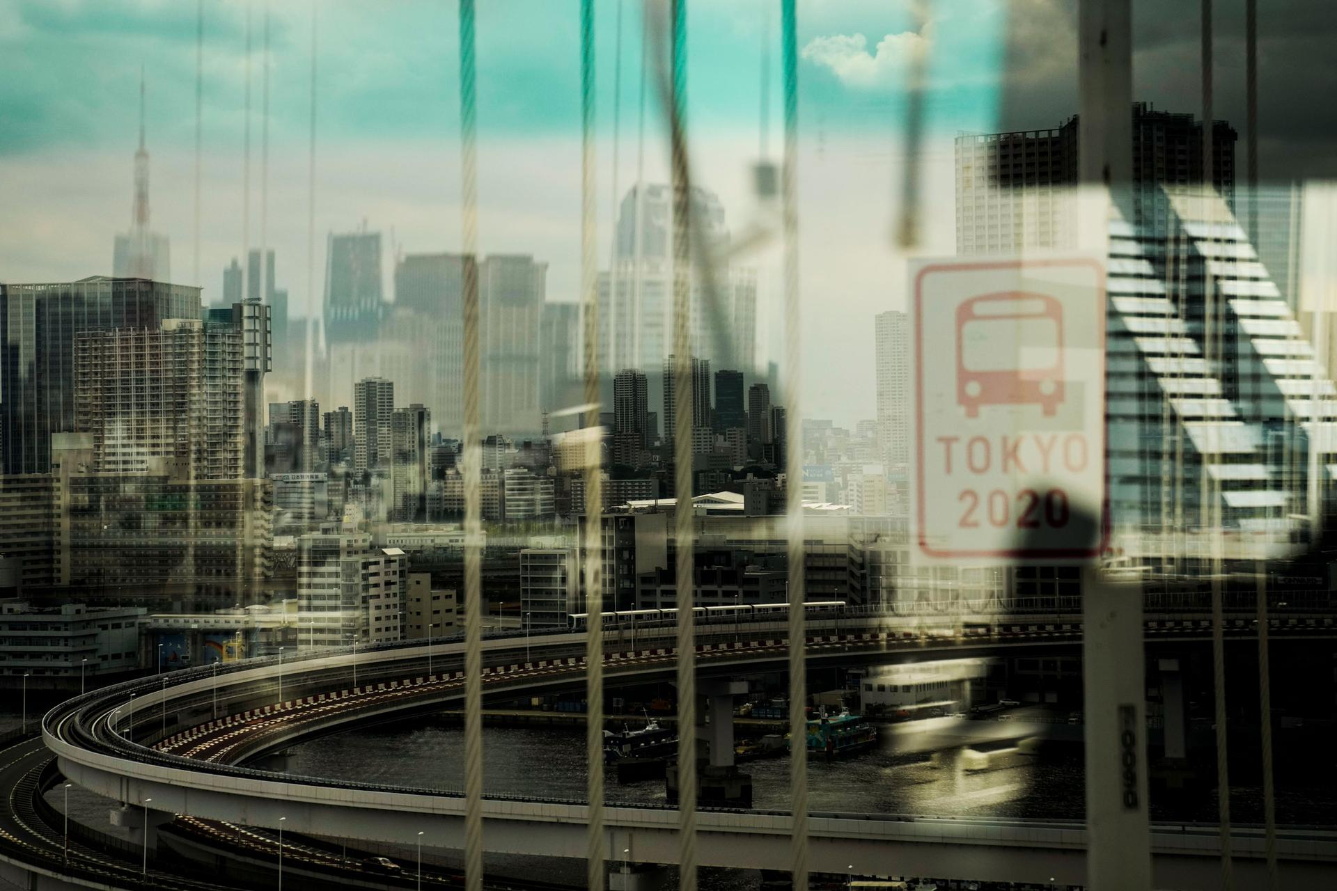 A major roadway and elevated train track along with the Tokyo skyline are shown blurred slightly via a bus window.