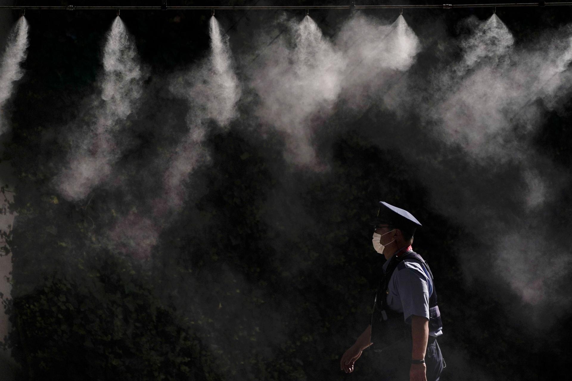 A police officer is shown wearing a white mask and walking under several misters spraying water.