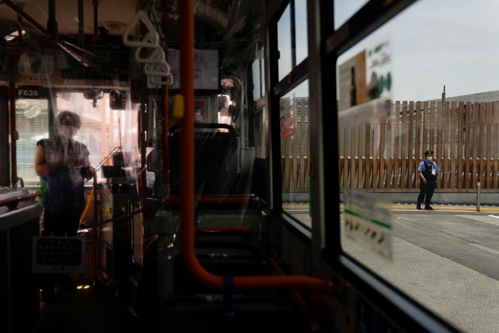 A police office is shown through the window of a bus standing guard in front of a metal barrier.
