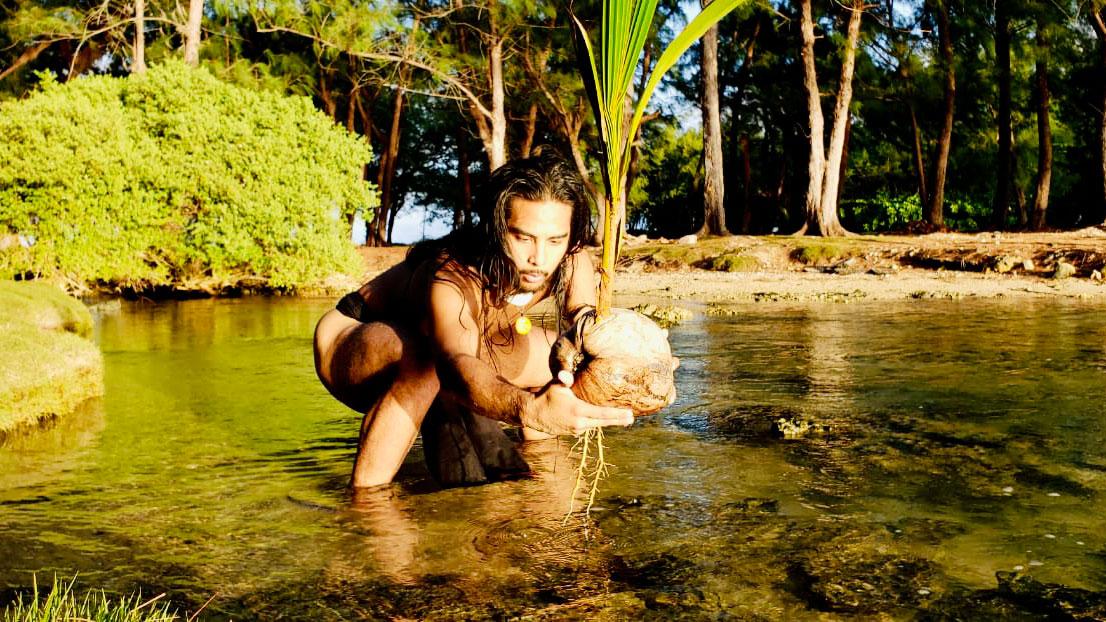 Dakota Camacho, dancer and musician, seen in a body of a water unclothed with long hair. 