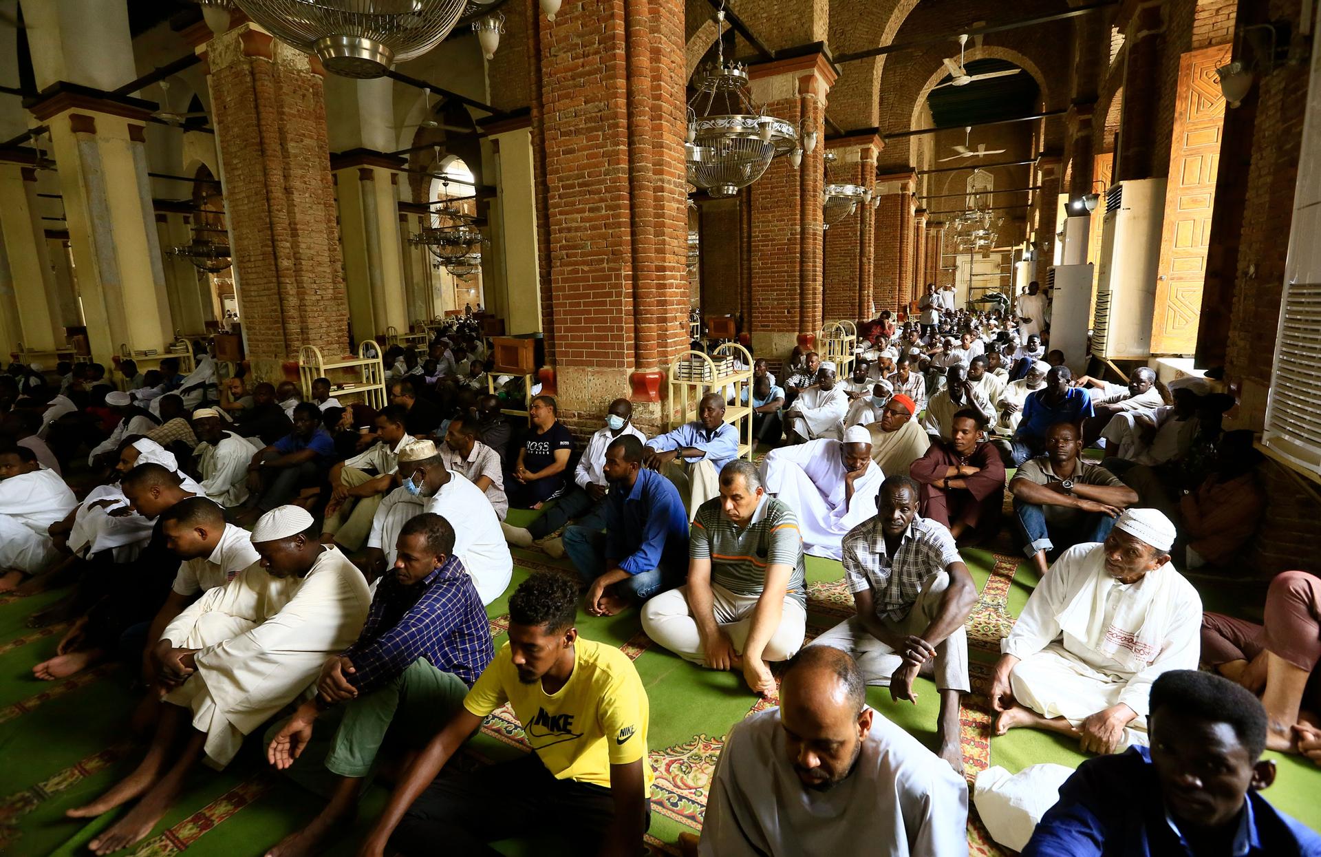 A large group of people are show sitting on the floor of the Grand Mosque with large brick columns down the middle.