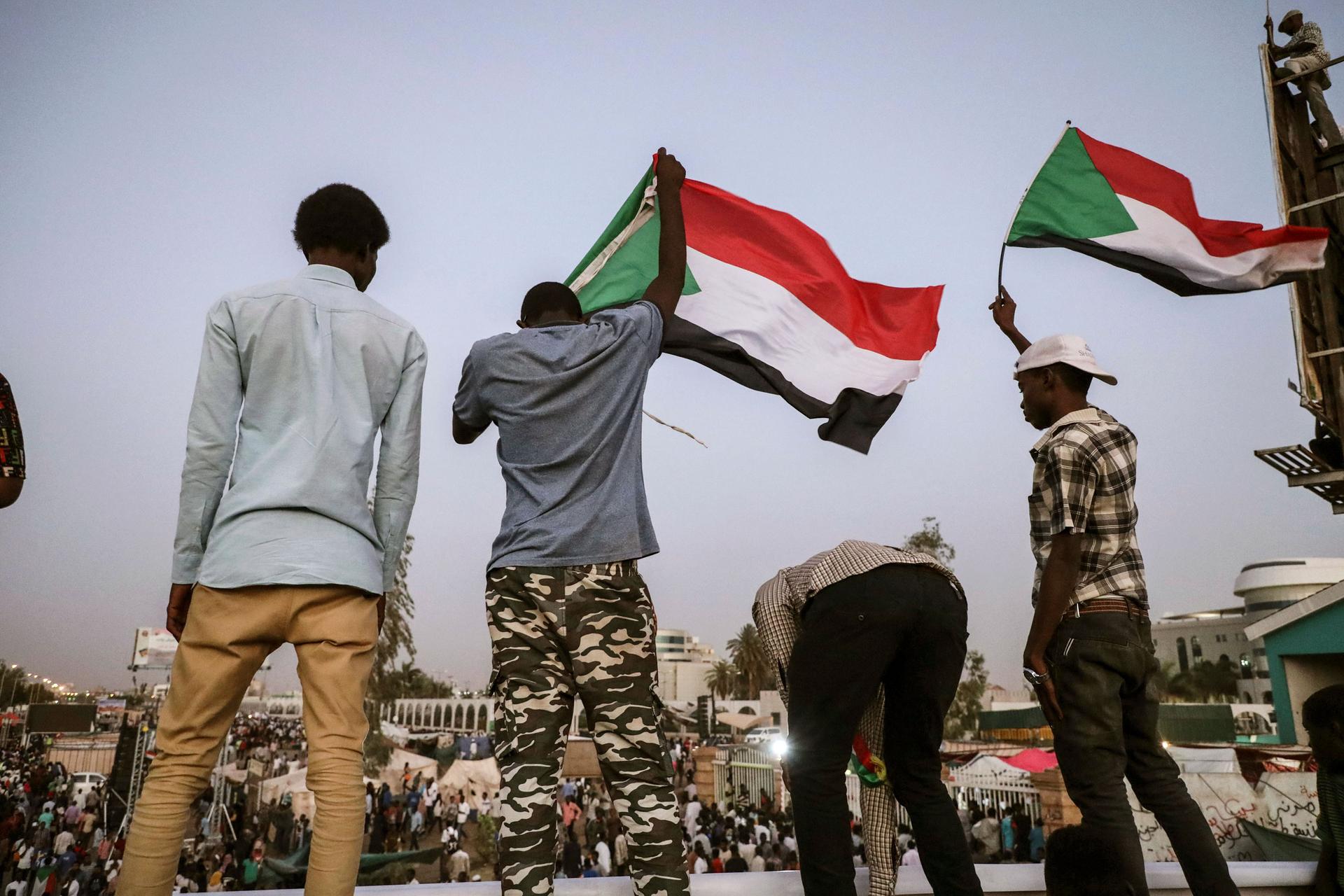 A group of four men are shown with two waving the Sudanese national flag.