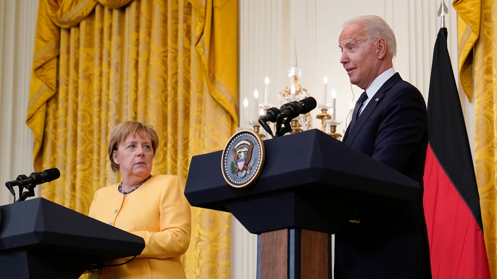 President Joe Biden and German Chancellor Angela Merkel are shown each standing behind podiums with several microphones on each stand.