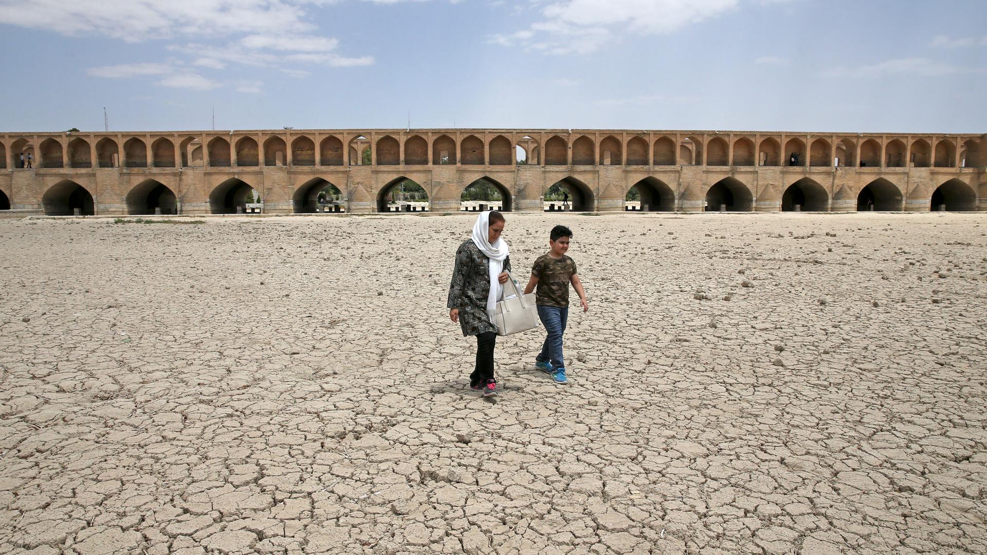 A woman and a boy walk on the dried up riverbed of the Zayandeh Roud river that no longer runs under the 400-year-old Si-o-seh Pol bridge, named for its 33 arches, in Isfahan, Iran