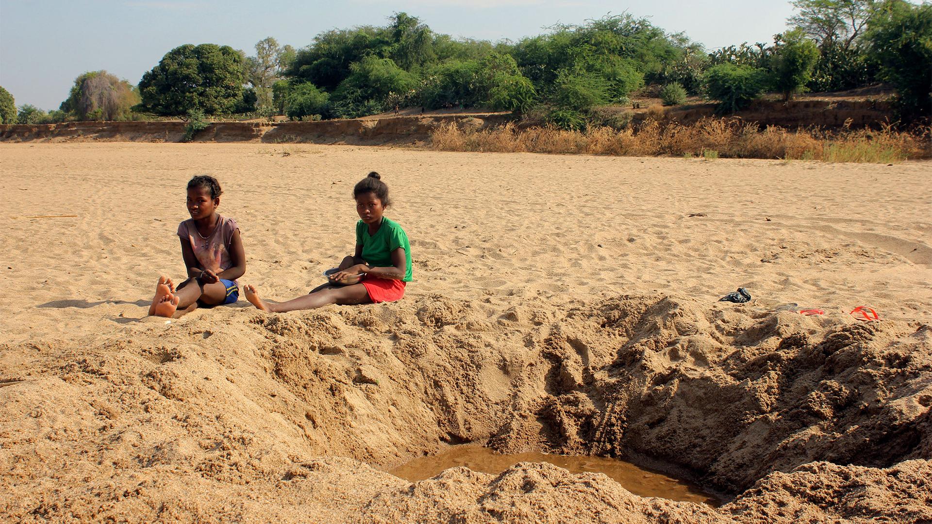 Children sit by a dug out water hole in a dry river bed in the remote village of Fenoarivo, Madagascar