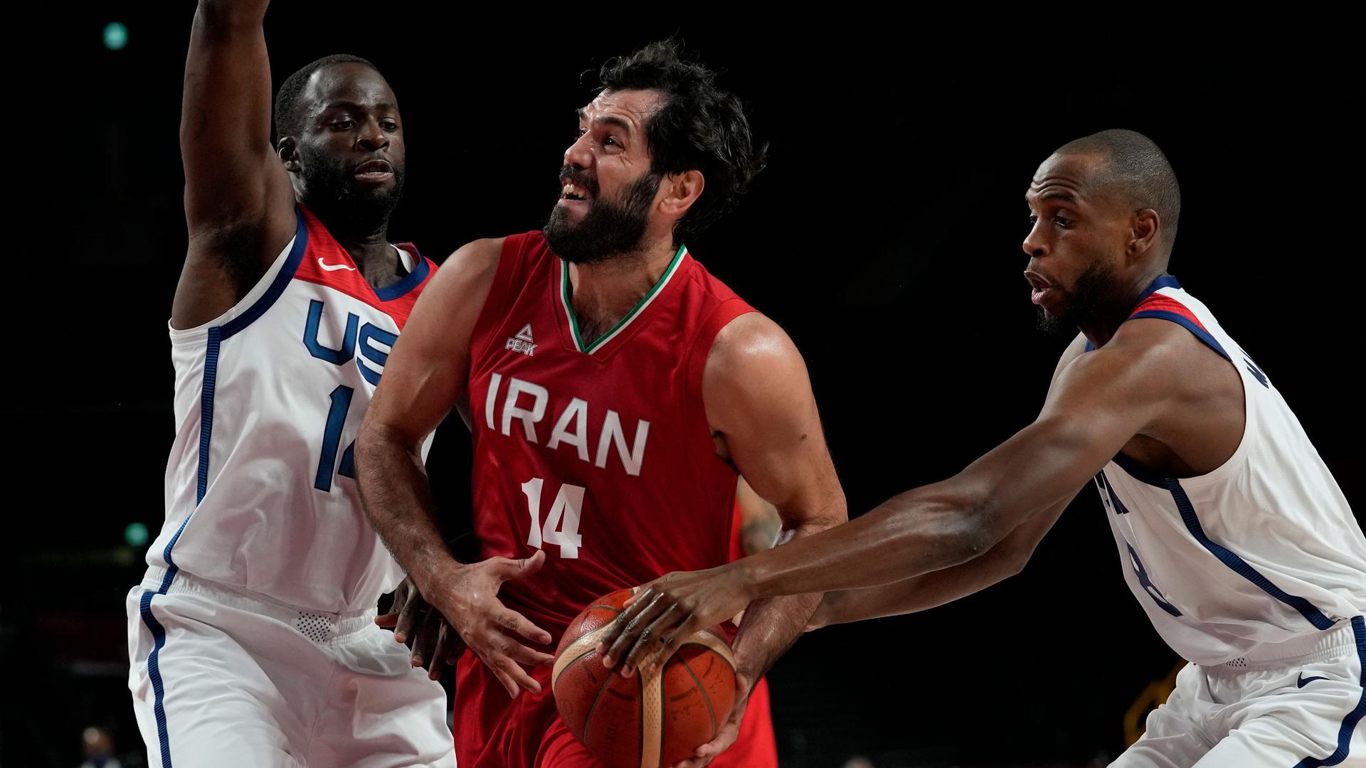 Two basketball players dressed in white US uniforms are shown on either side of a player wearing a red Iranian uniform.