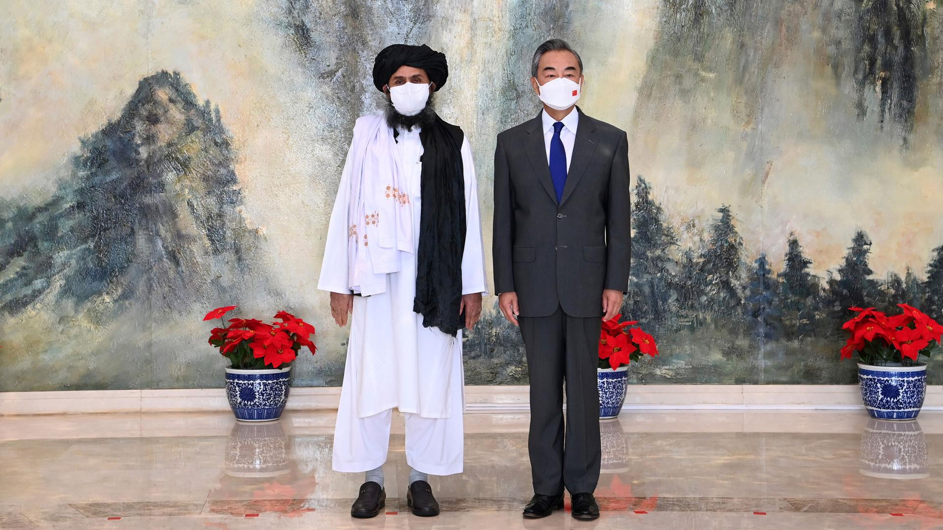 Taliban co-founder Mullah Abdul Ghani Baradar is shown wearing traditional white robes while standing next to and Chinese Foreign Minister Wang Yi wearing a suit.