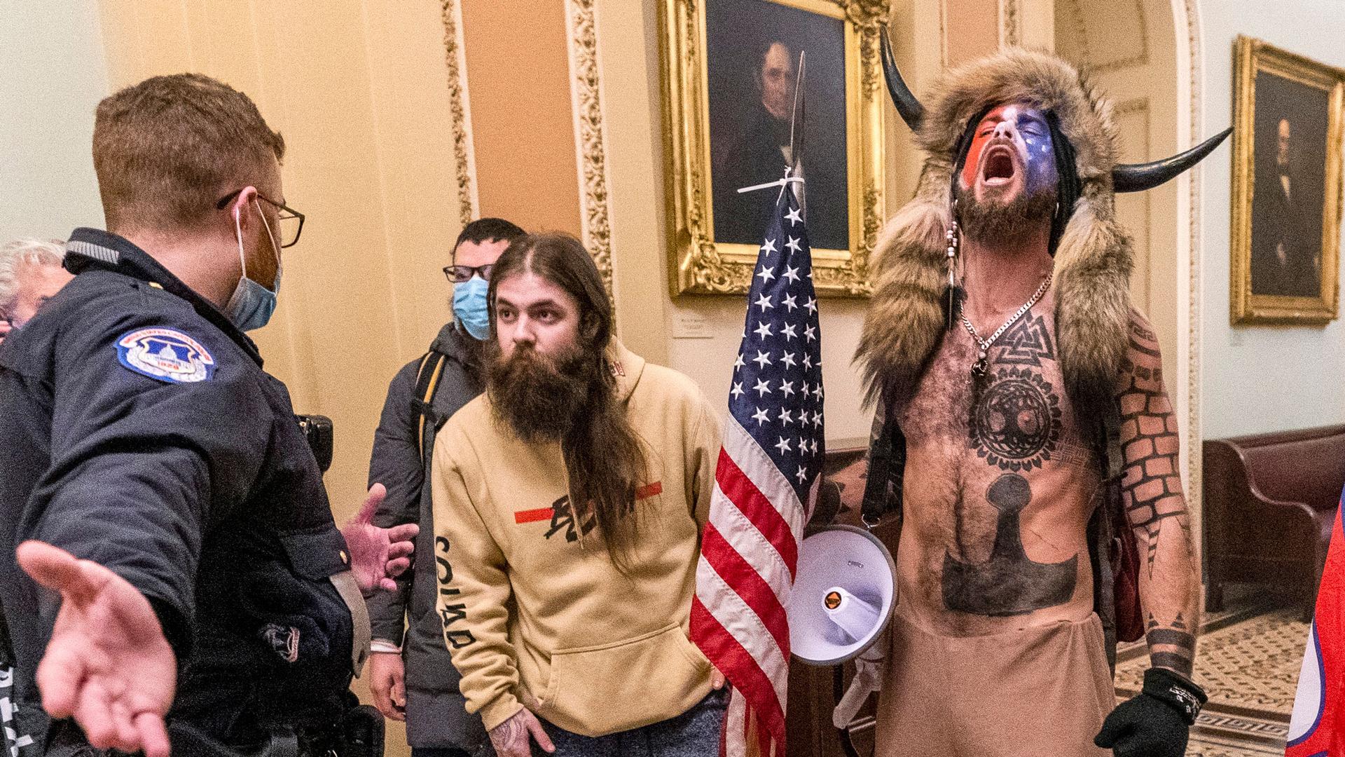 Supporters of President Donald Trump, including Jacob Chansley, right with fur hat, are confronted by US Capitol Police officers outside the Senate Chamber inside the Capitol in Washington. Many of those who stormed the Ca