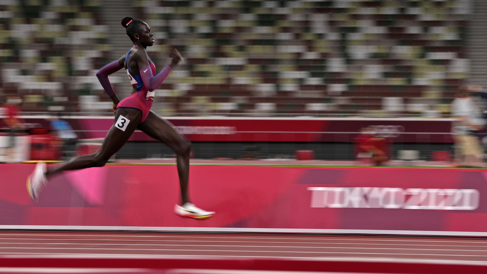 Athing Mu is shown mid-stride on the track in blurred motion.