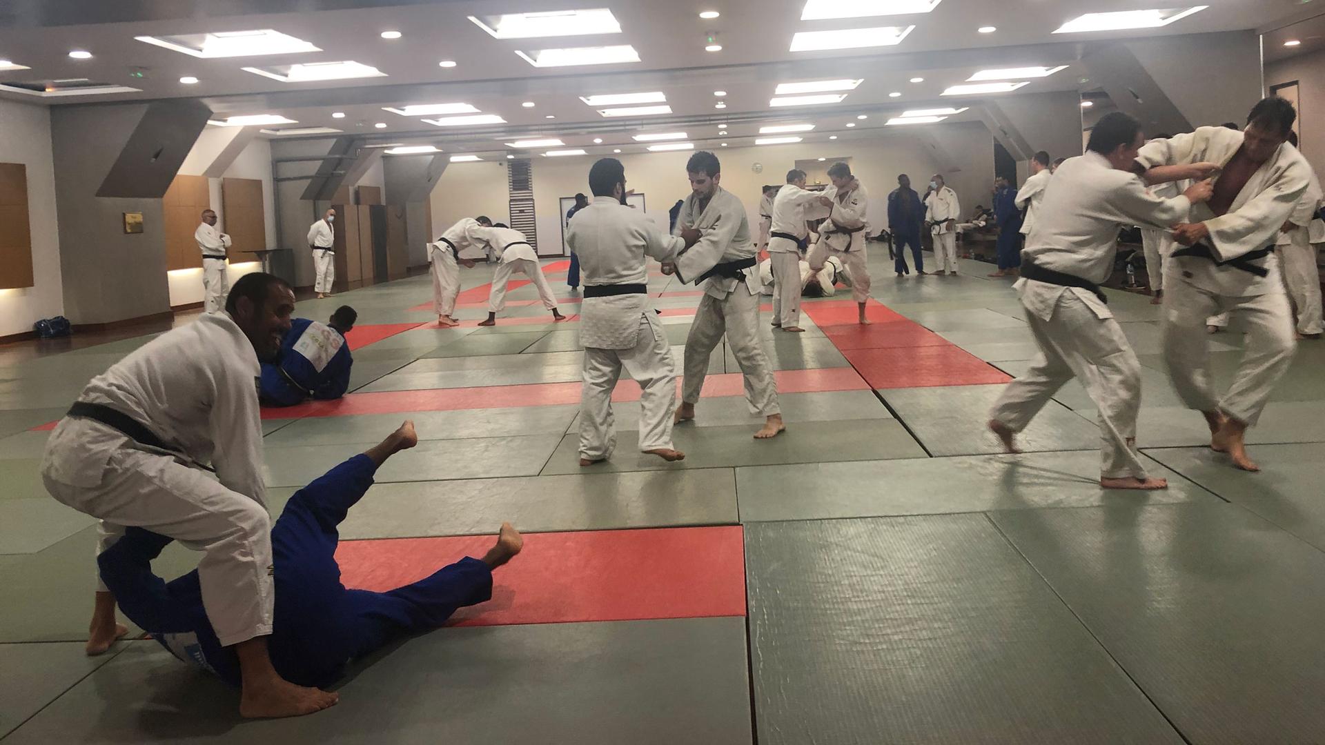A group of 40 men of all ages wear a mix of white and blue judogis — the traditional judo uniform. Most are black belts.