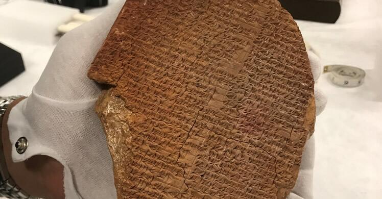 White-gloved hand holds ancient artifact known as the Gilgamesh Dream Tablet. 