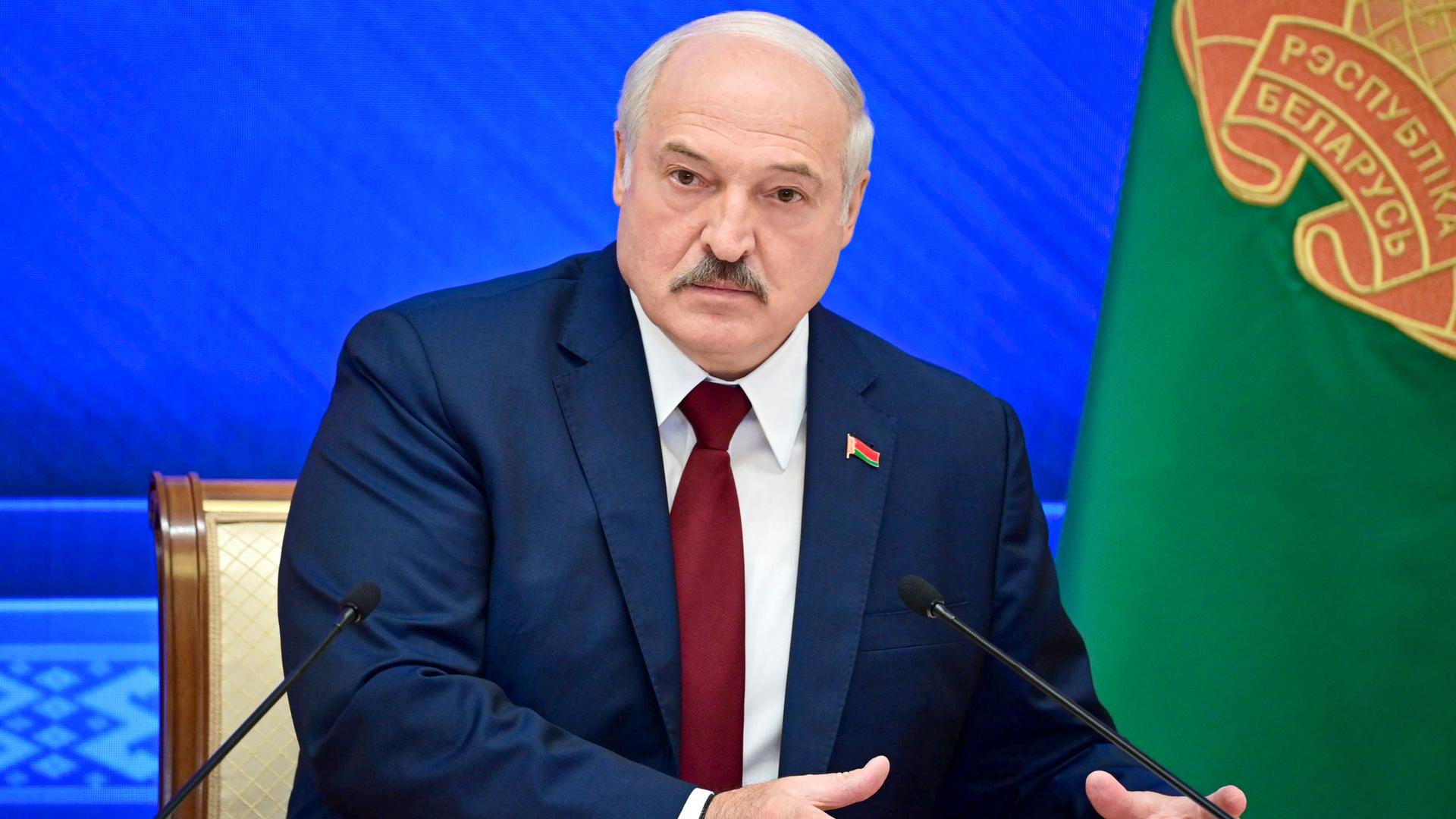 Belarusian President Alexander Lukashenko is shown sitting while wearing a blue suit jacket with a red tie.