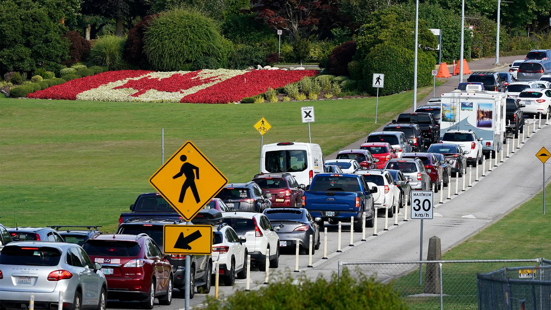 A line of vehicles wait to cross the Canadian border in view of a Canadian flag made of flowers