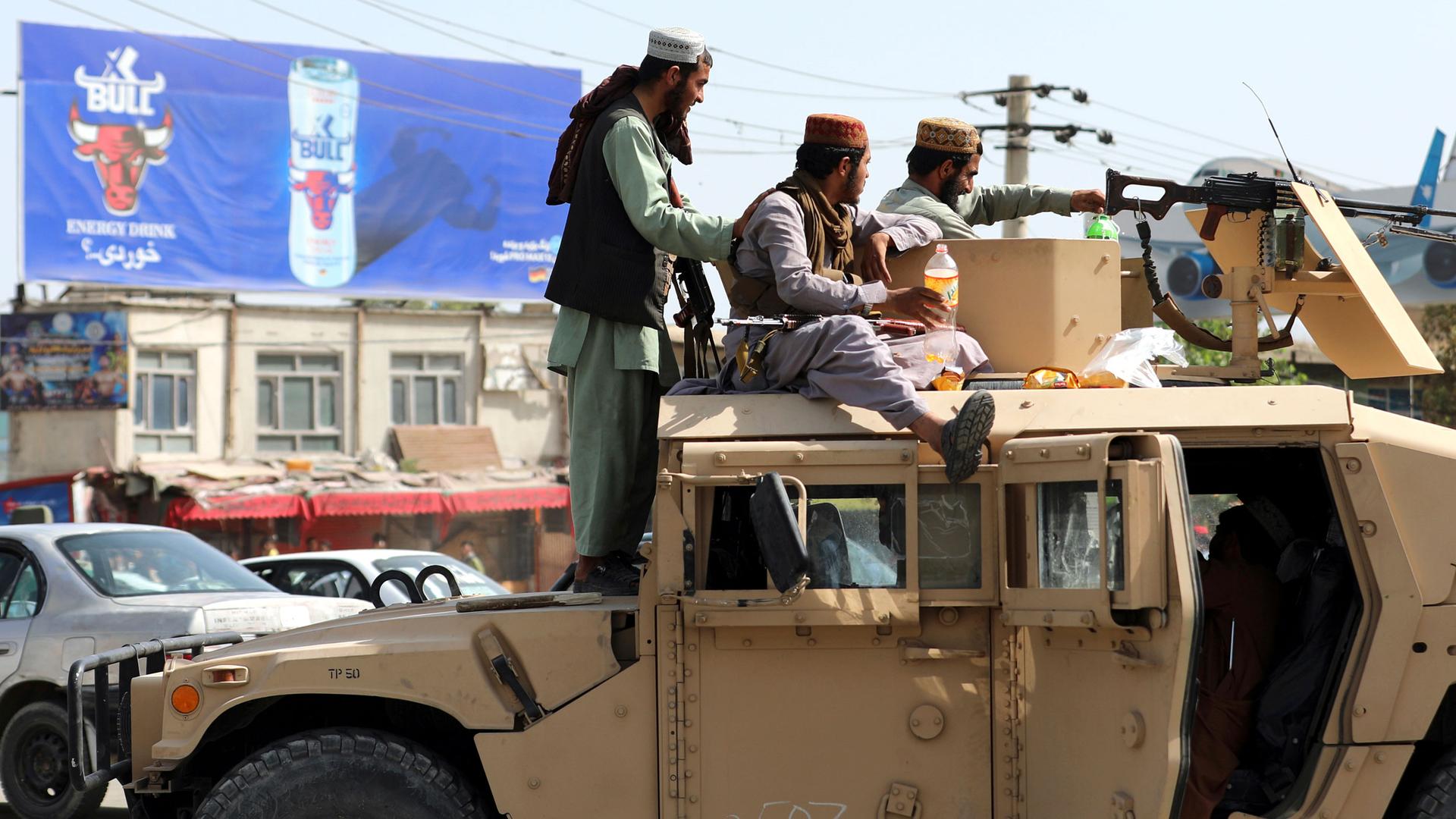 Several members of the Taliban are shown atop a tan-color Humvee with a large weapon on top.
