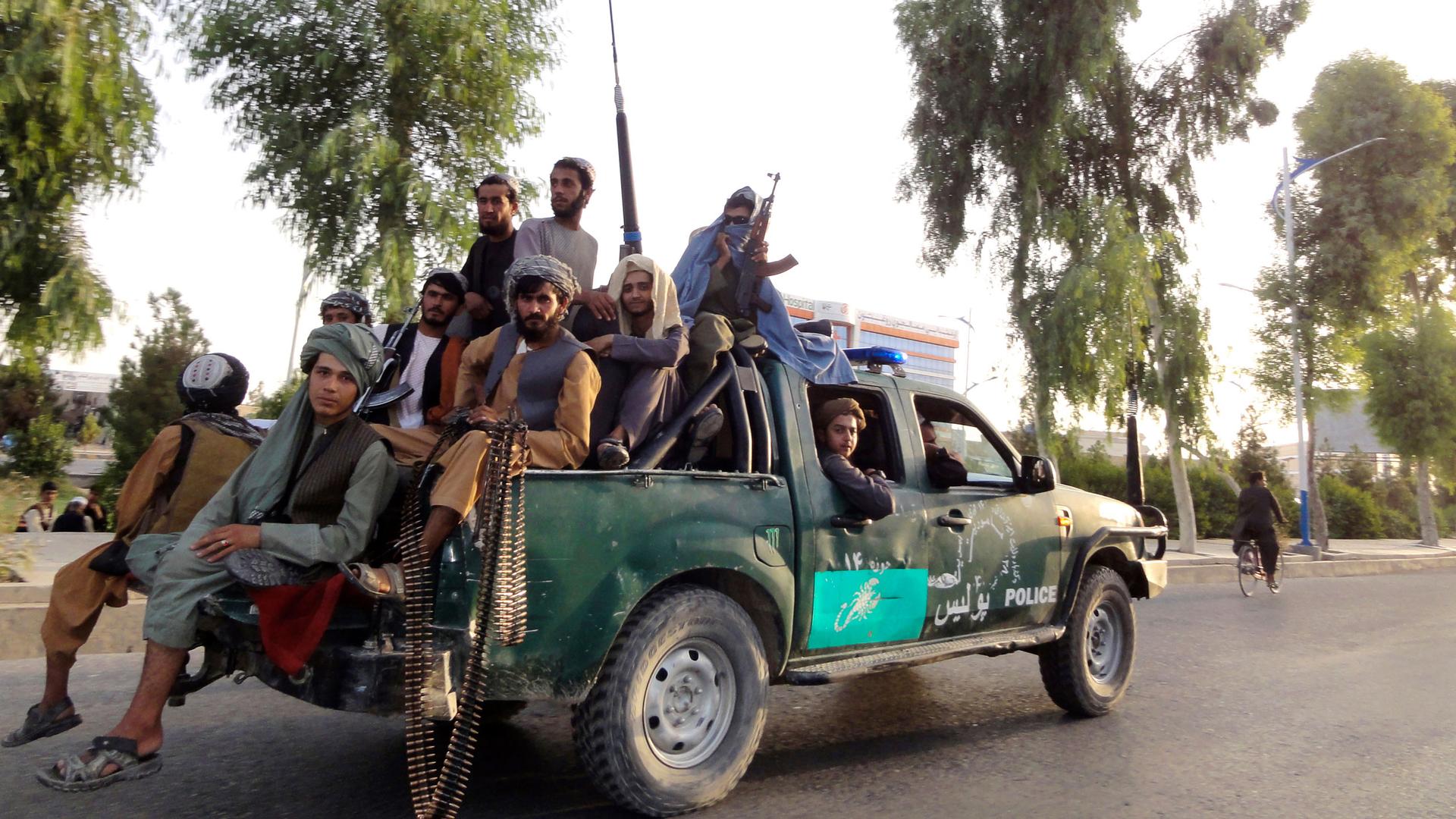 Several Taliban fighters are shown sitting in the back of a pickup truck, several holding weapons.