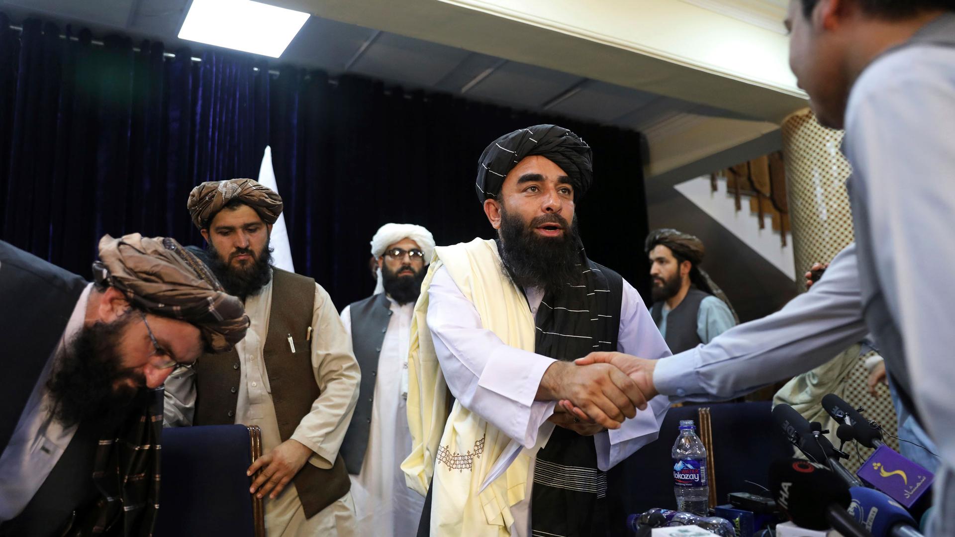 Taliban spokesman Zabihullah Mujahid shakes hand with a journalist after his first news conference, in Kabul, Afghanistan, Tuesday, Aug. 17, 2021. 