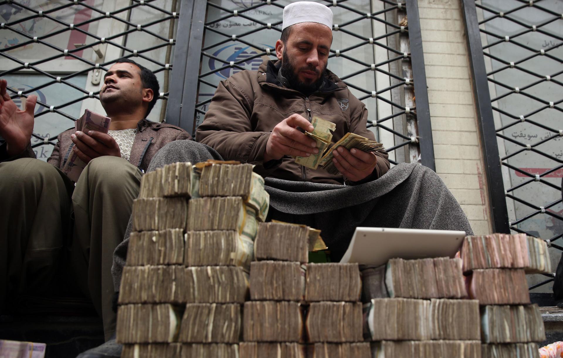 In this Monday, Jan. 12, 2015, file photo, An Afghan money changer, right, counts a pile of currency at the Money and Exchange Market in Kabul.