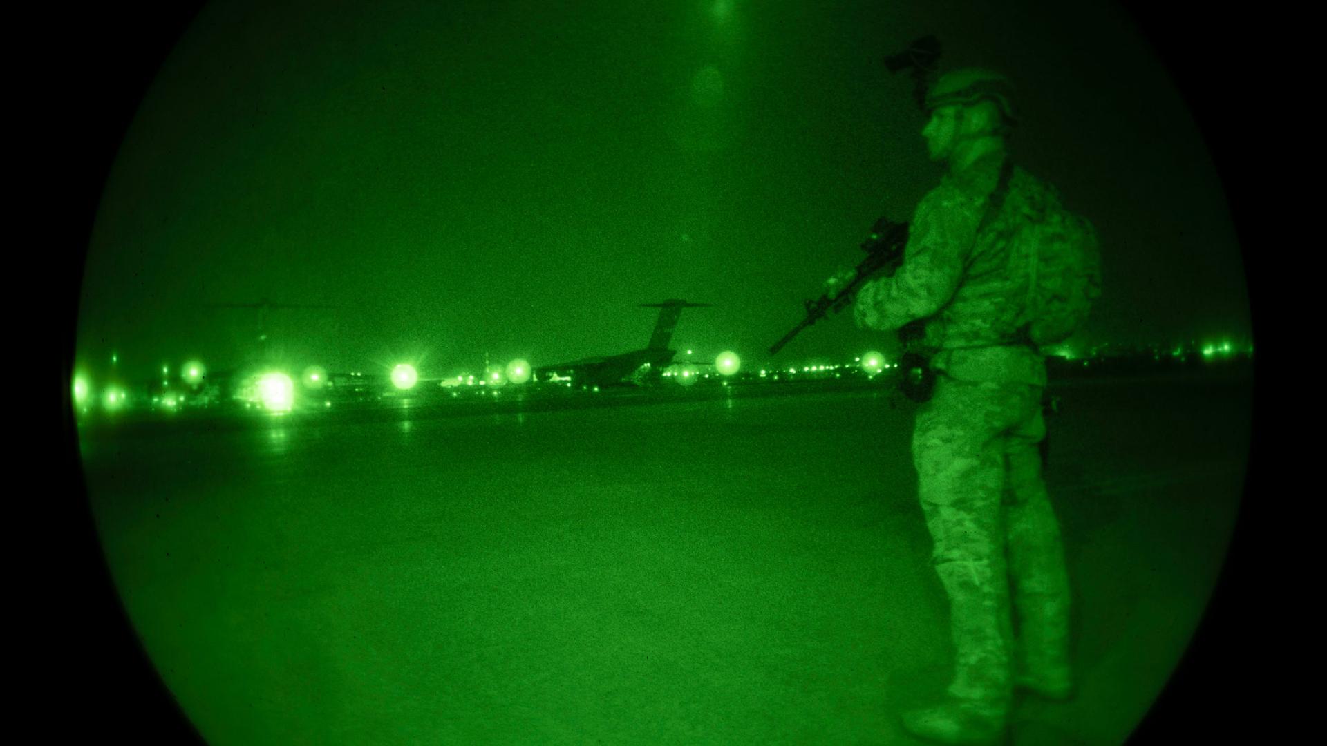 In this Aug. 22, 2021, image provided by the US Air Force and made through a night vision scope, a US Air Force security forces raven, assigned to the 816th Expeditionary Airlift Squadron, maintains a cordon around a US Air Force C-17 Globemaster III in s
