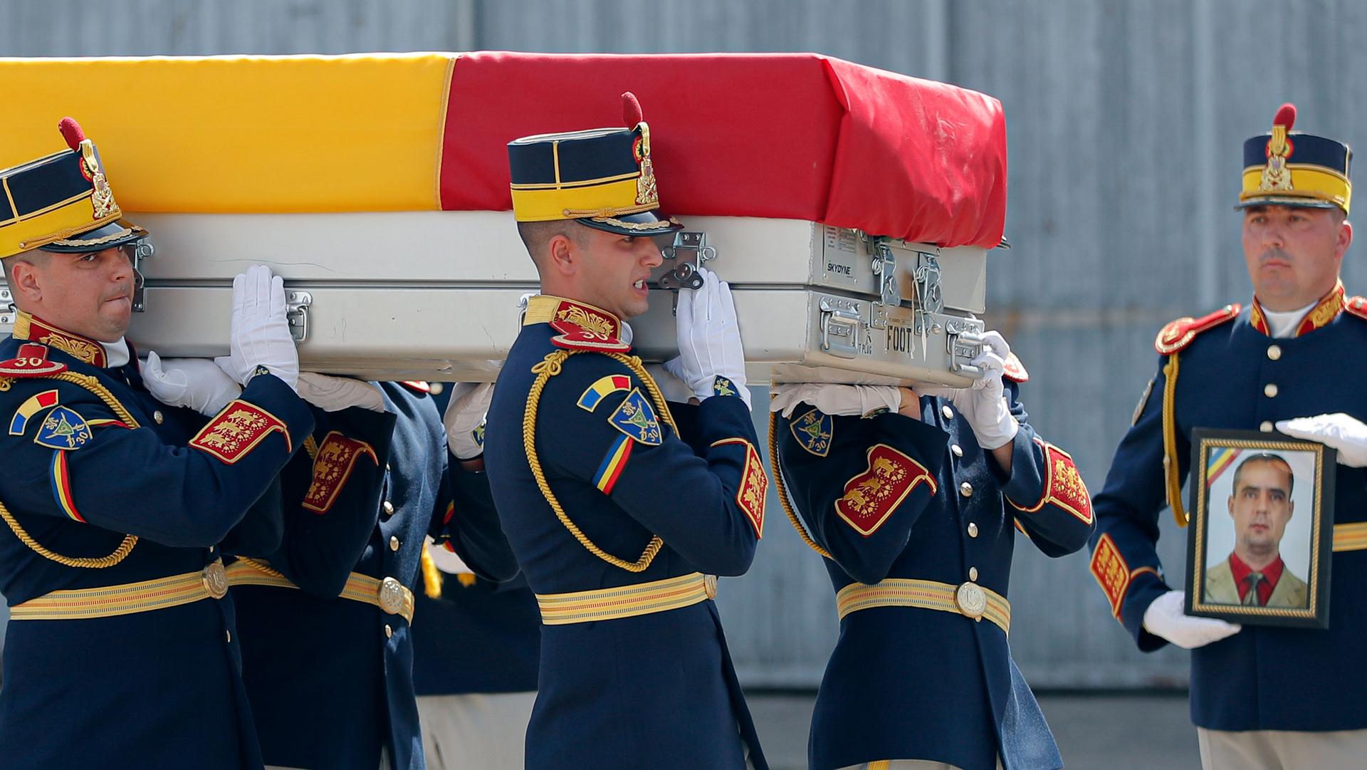 Honor guard soldiers carry the coffin of Vasile Raduna, seen in the photo on the right, during the ceremony for the repatriation his and of Corp. Ciprian-Stefan Polschi's body from Afghanistan, in Bucharest, Romania, Tuesday, Sept. 10, 2019. 