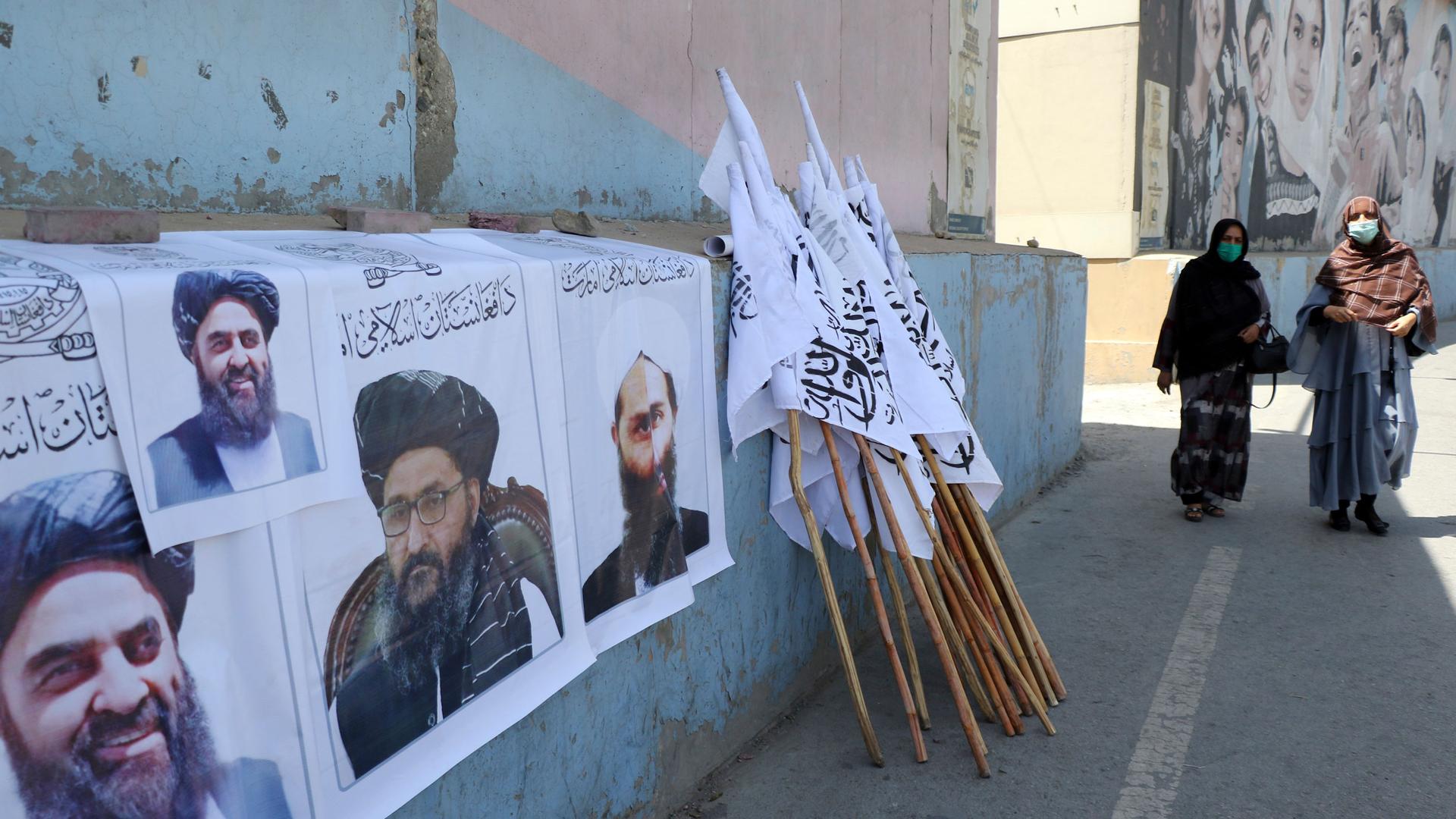 Afghan women walk by posters of Taliban leaders and flags in Kabul, Afghanistan, Wednesday, Aug. 25. 2021.