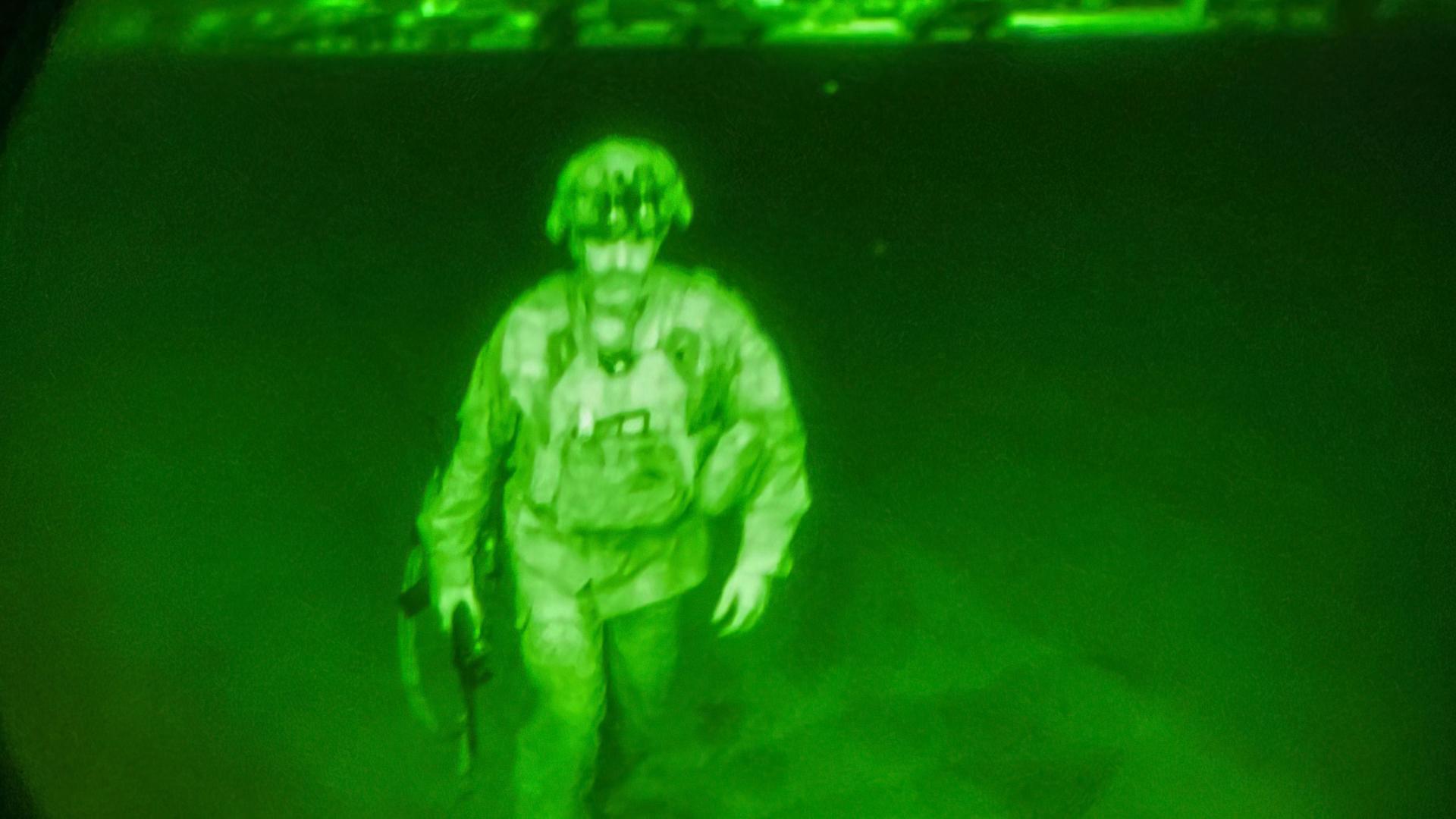 A US military officer is shown wearing full combat gear under the green light of a night goggle lens.