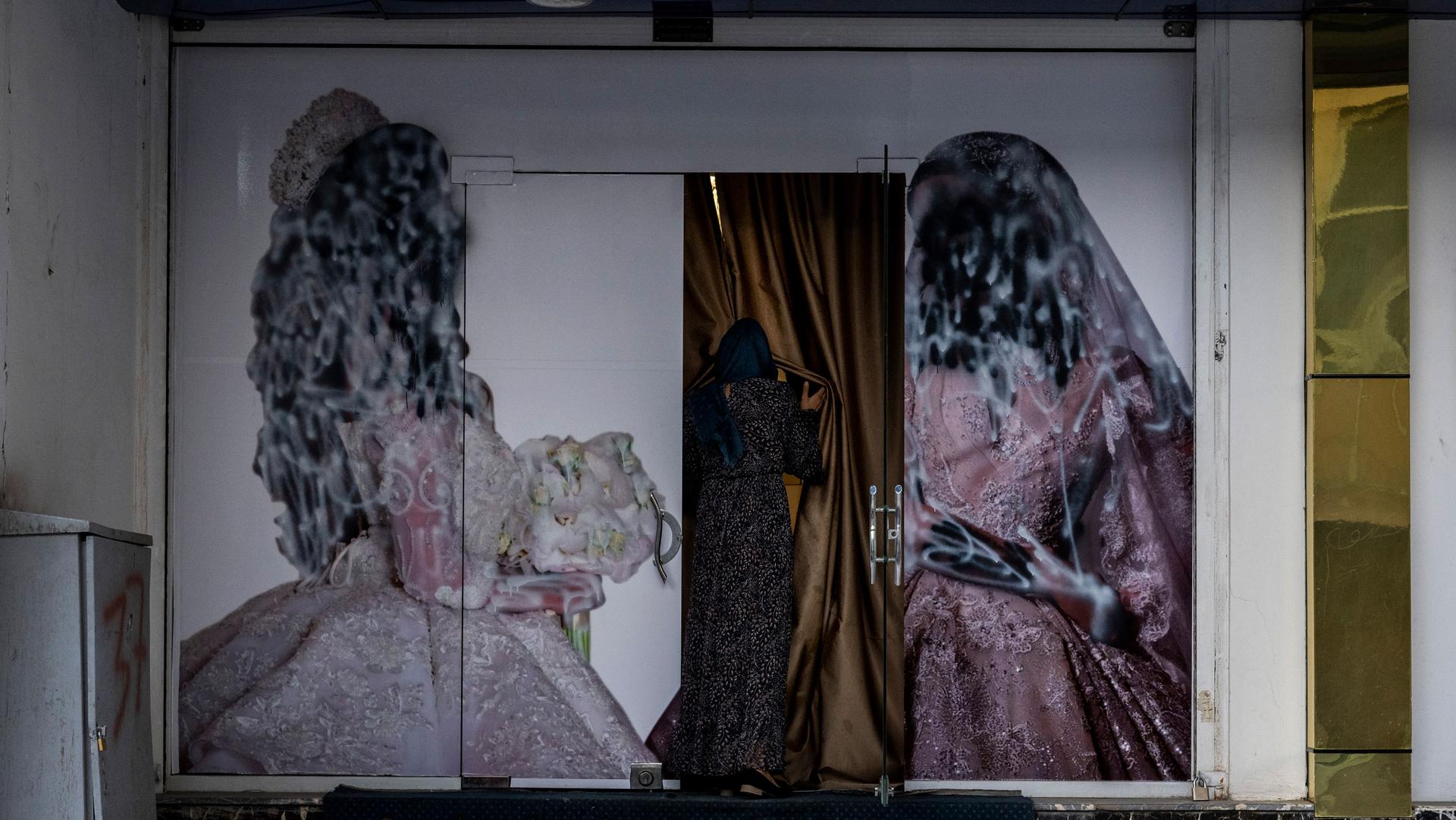 A woman is shown holding back a curtain and entering a salon with painted over pictures of women on either side of the doorway.