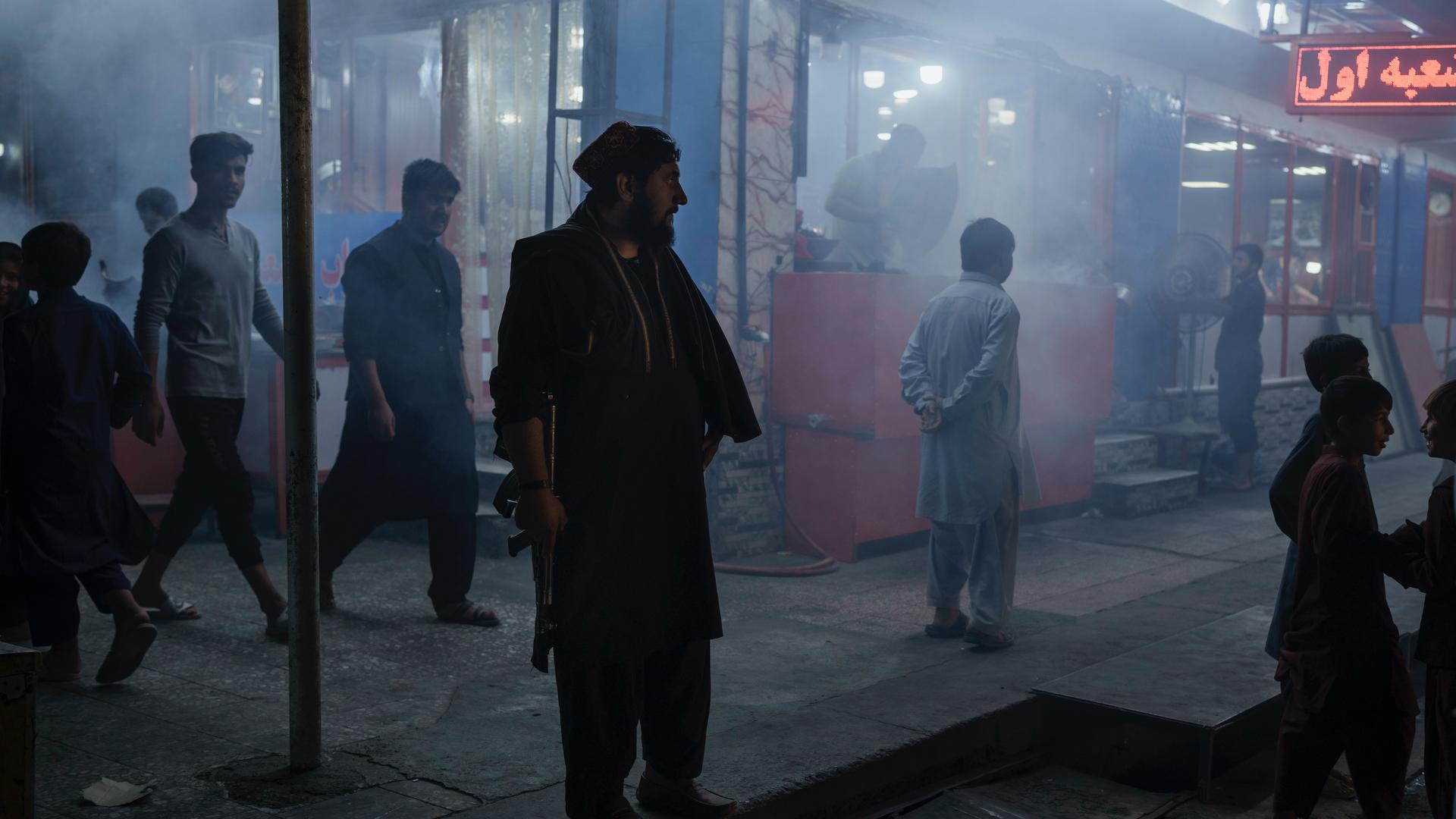A Taliban fighter stands in the corner of a busy street at night in Kabul, Afghanistan, Sept. 17, 2021.