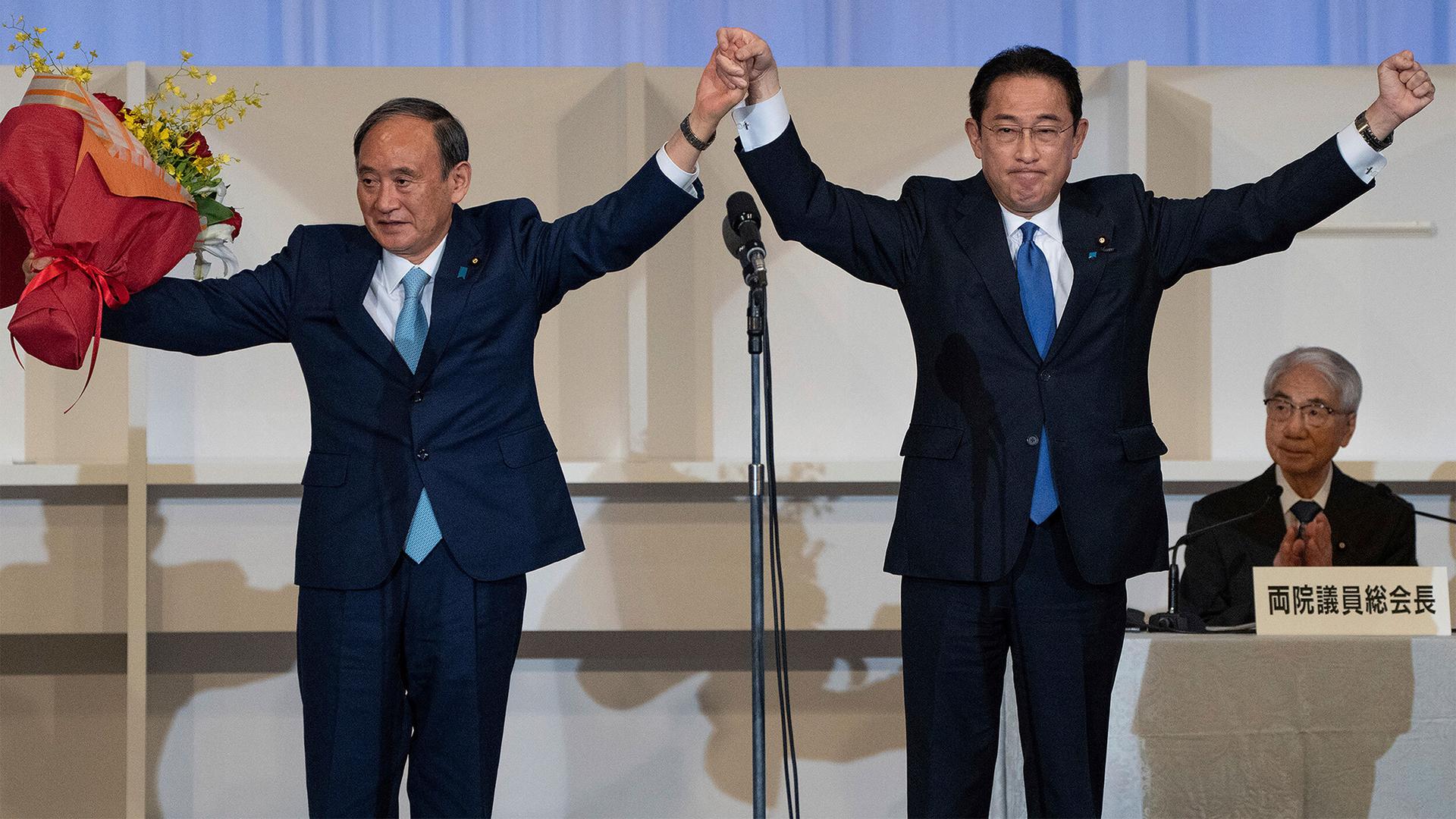 Fumio Kishida, right, is shown with his arms raised celebrating with Yoshihide Suga who is standing next to him.