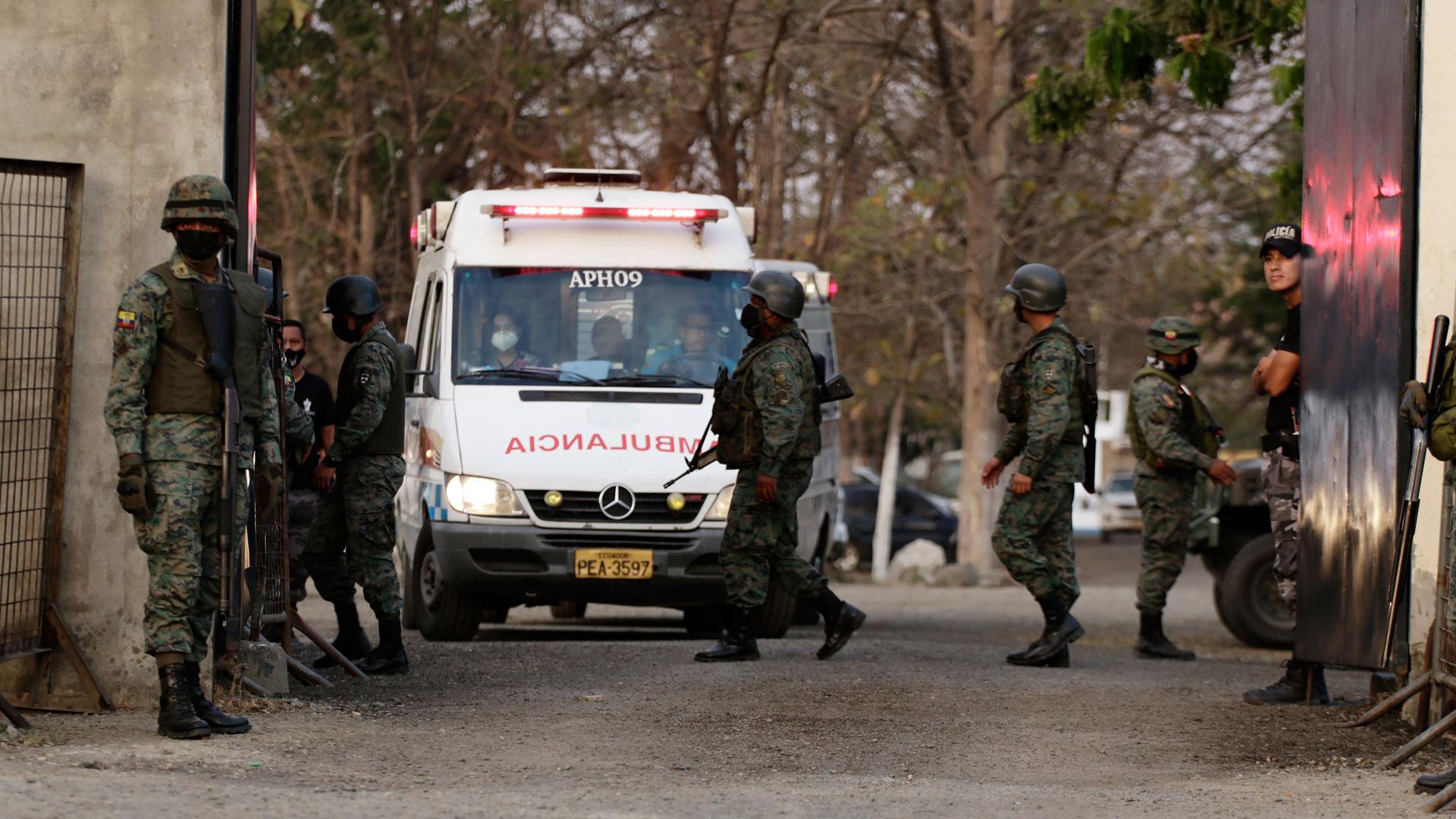 A white ambulance is shown from the front with several people wearing military fatigues and carrying weapons standing nearby.