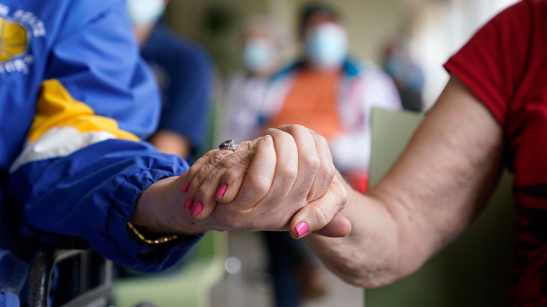 Residents Ken Fishman, 81, left, and Esther Wallach, 82, right, hold hands as they wait in line for the Pfizer-BioNTech COVID-19 vaccine at the The Palace assisted living facility in Coral Gables, Florida