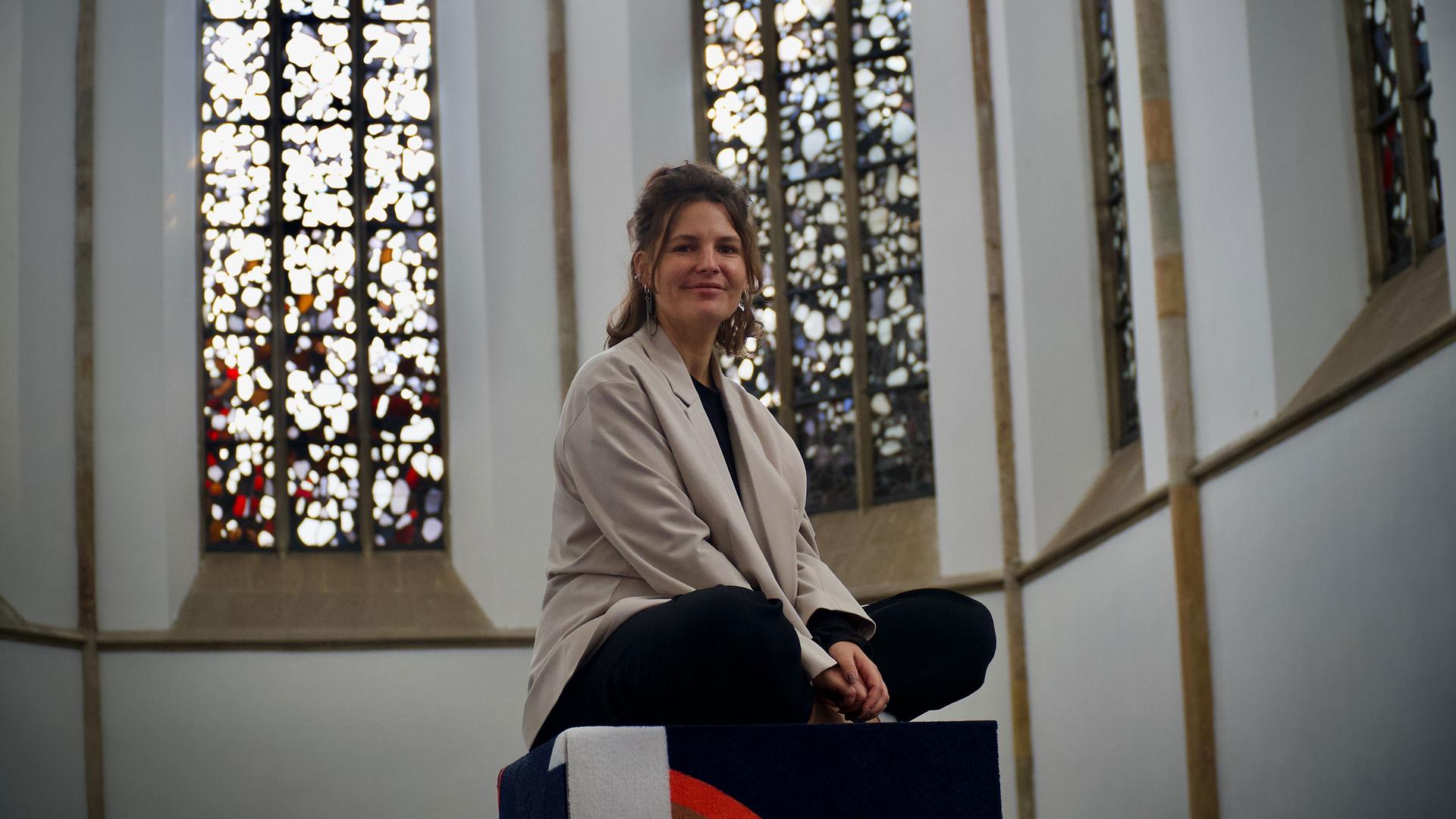 Kunsthalle Osnabrück co-director Anna Jehle sits near colorful stained-glass windows inside a church.