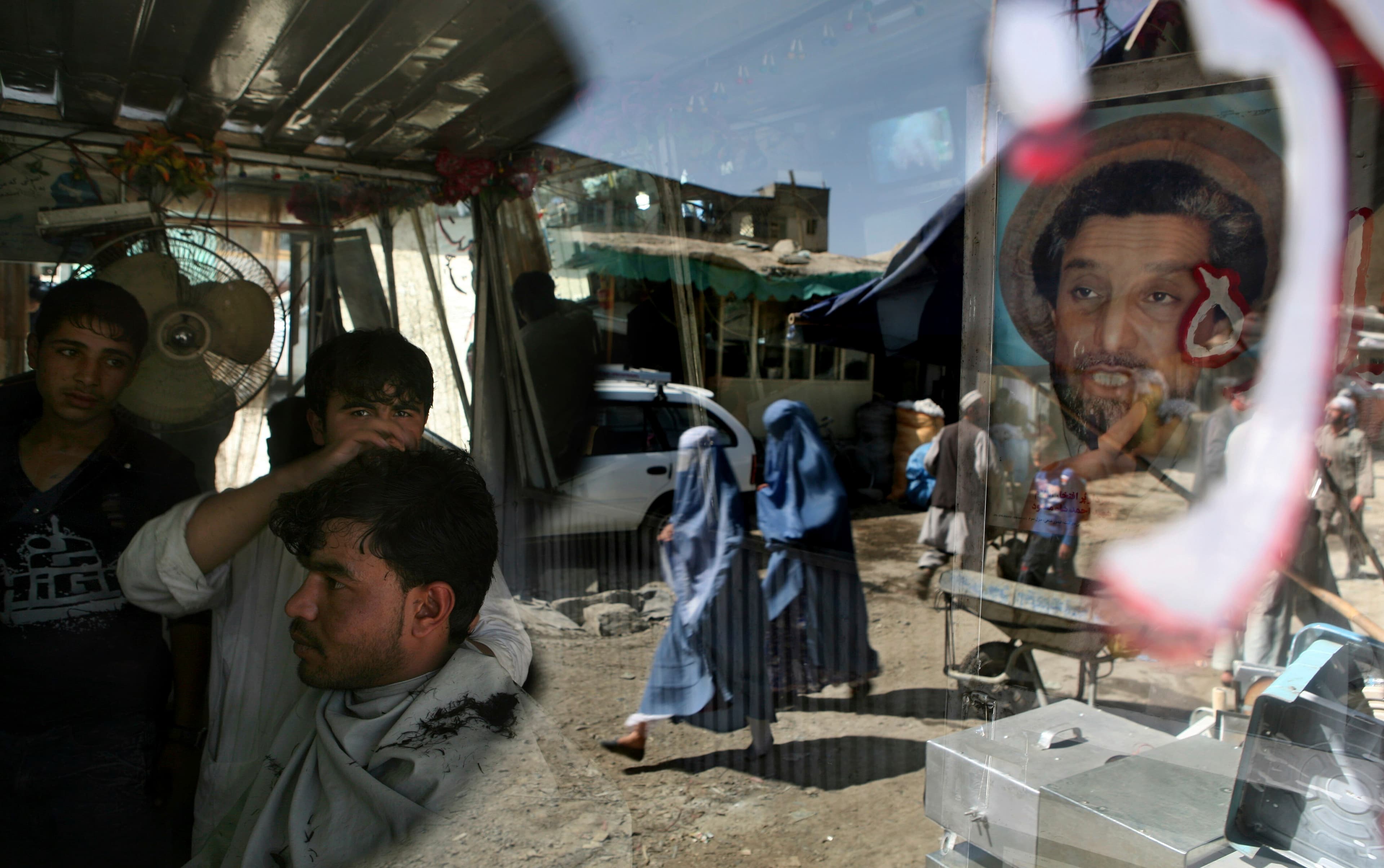 An Afghan barber works on a customer in his shop as a portrait of Afghanistan national hero Ahmad Shah Massoud adorns its door in Kabul, Afghanistan, on Sept. 29, 2009.