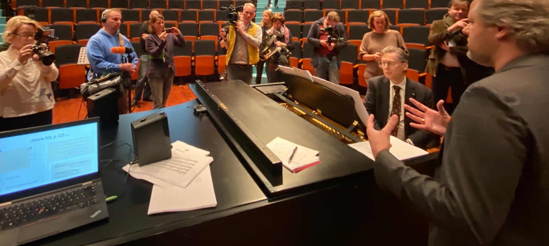 Group of people stand around a pianist in an auditorium
