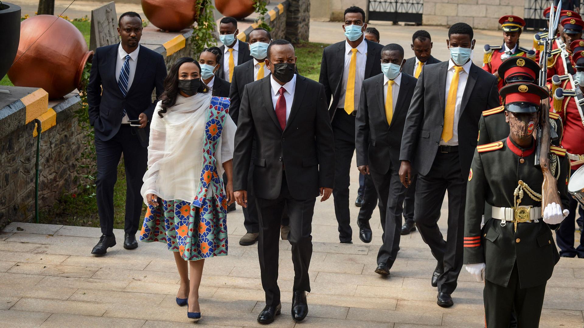 Ethiopia's Prime Minister Abiy Ahmed is shown wearing a suit a face mask while walking next to First Lady Zinash Tayachew who is wearing a white and flower print dress.