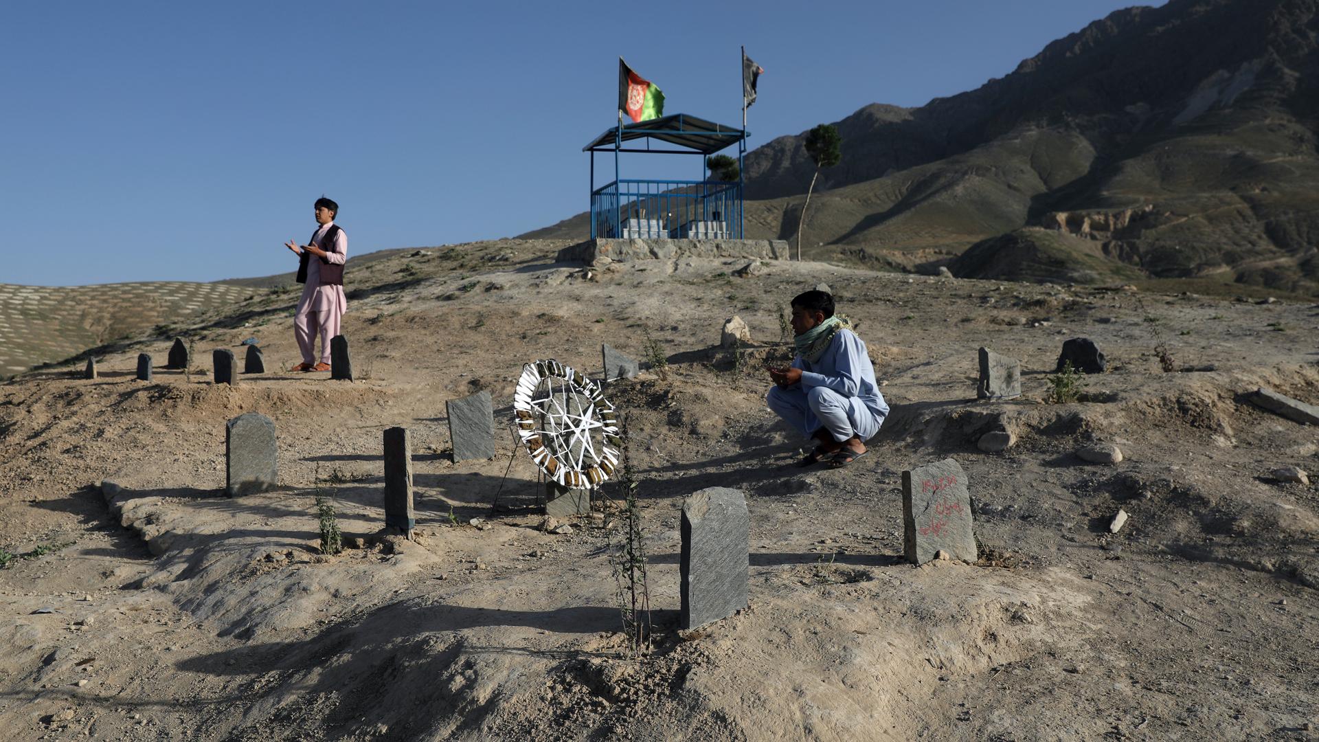 Afghan men pray near the grave of their relatives killed in bombings near Syed Al-Shahada School last month at a cemetery on the outskirts of Kabul, Afghanistan, June 2, 2021.